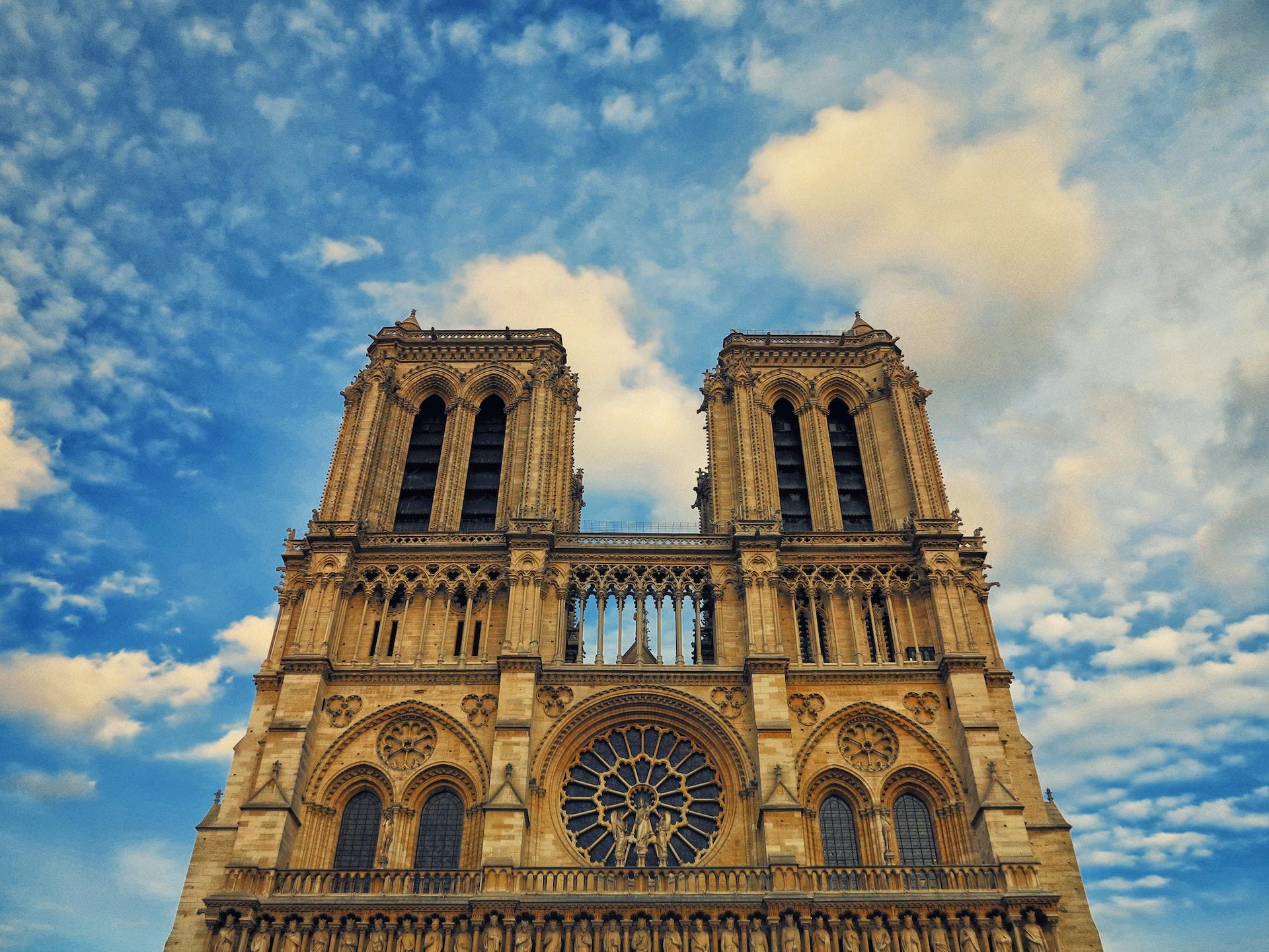 Notre Dame sett nedenfra med blå himmel og litt skyer i bakgrunnen.