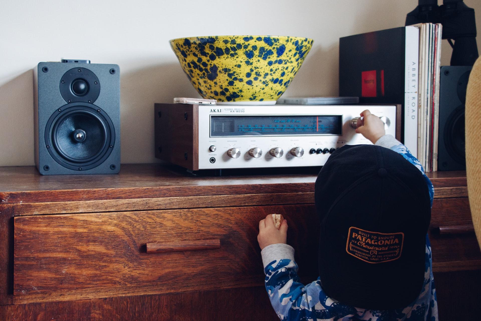 Liten gutt med caps bak fram skrur på en radio som står på en kommode.