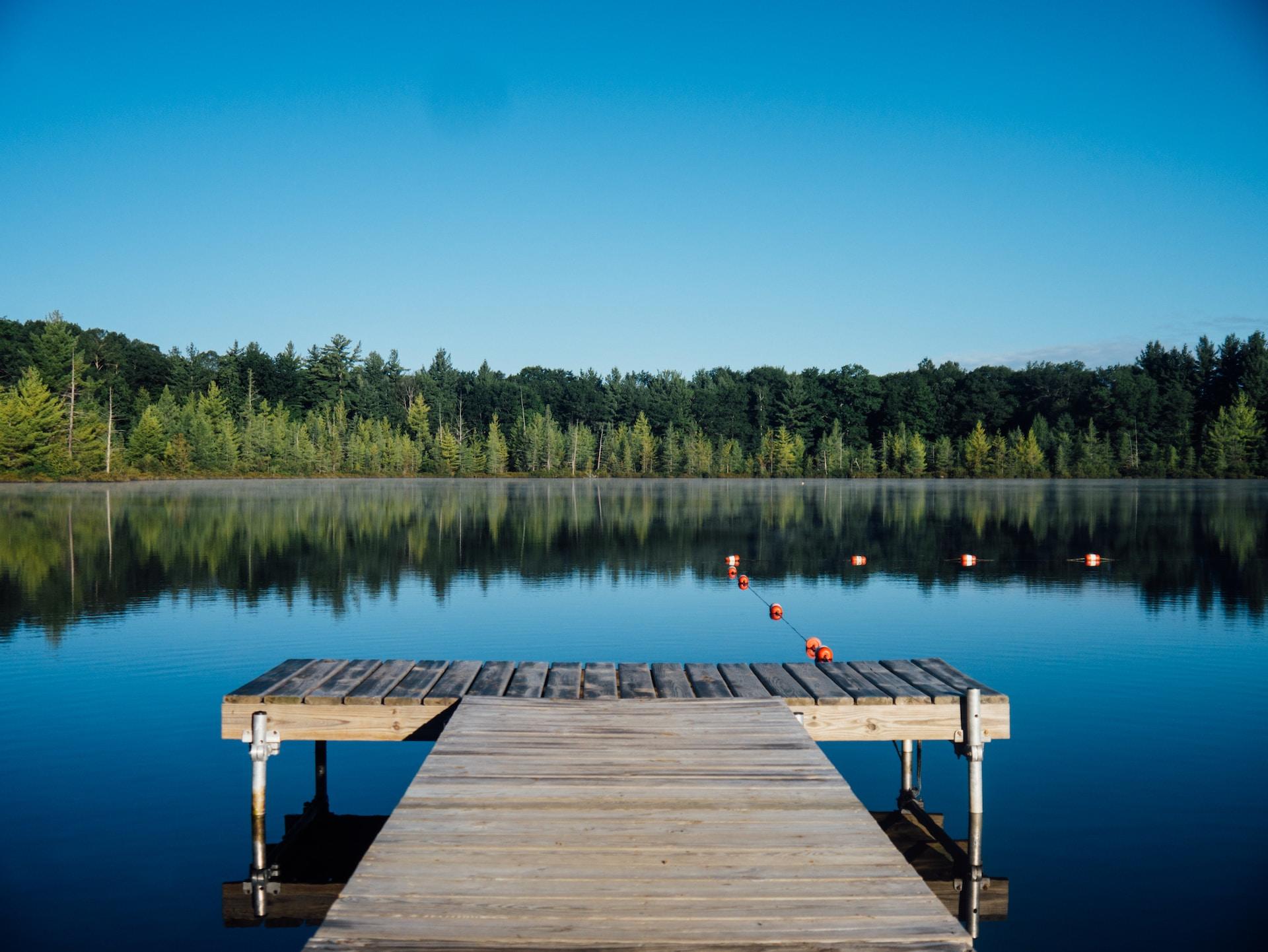 En brun trebrygge ved en liten innsjø omkranset av tett, grønn skog.