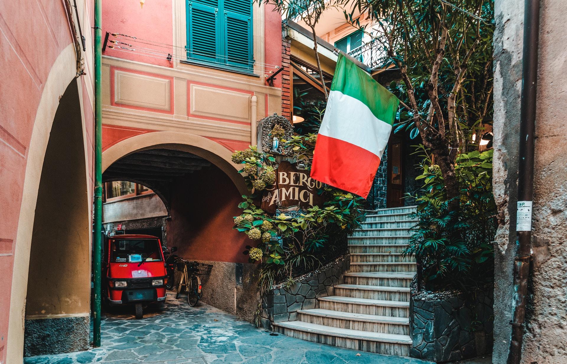 Liten italiensk by med rosa bygning, italiensk flagg hengende på veggen, og liten rød bil.