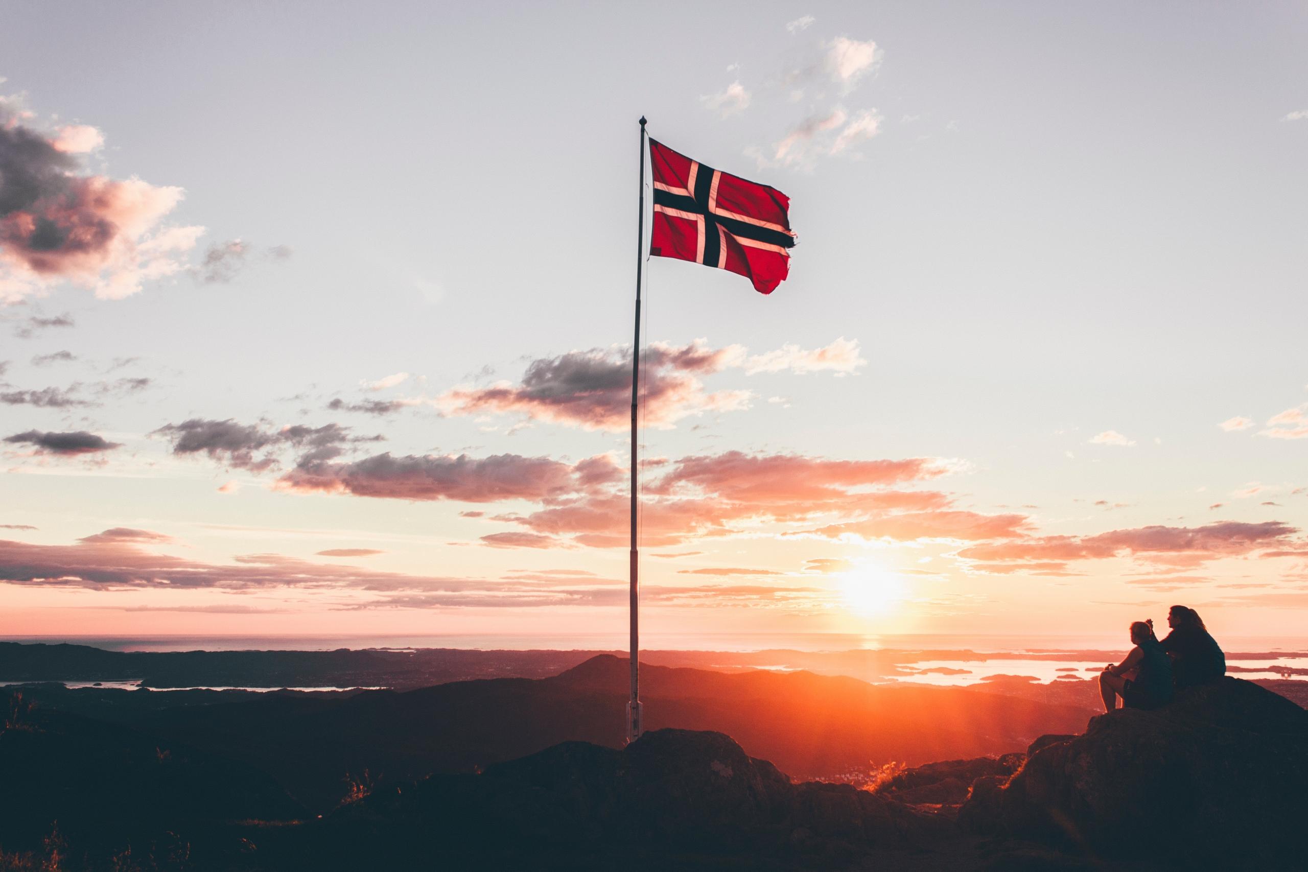 Det norske flagg blåser i vinden i solnedgangen