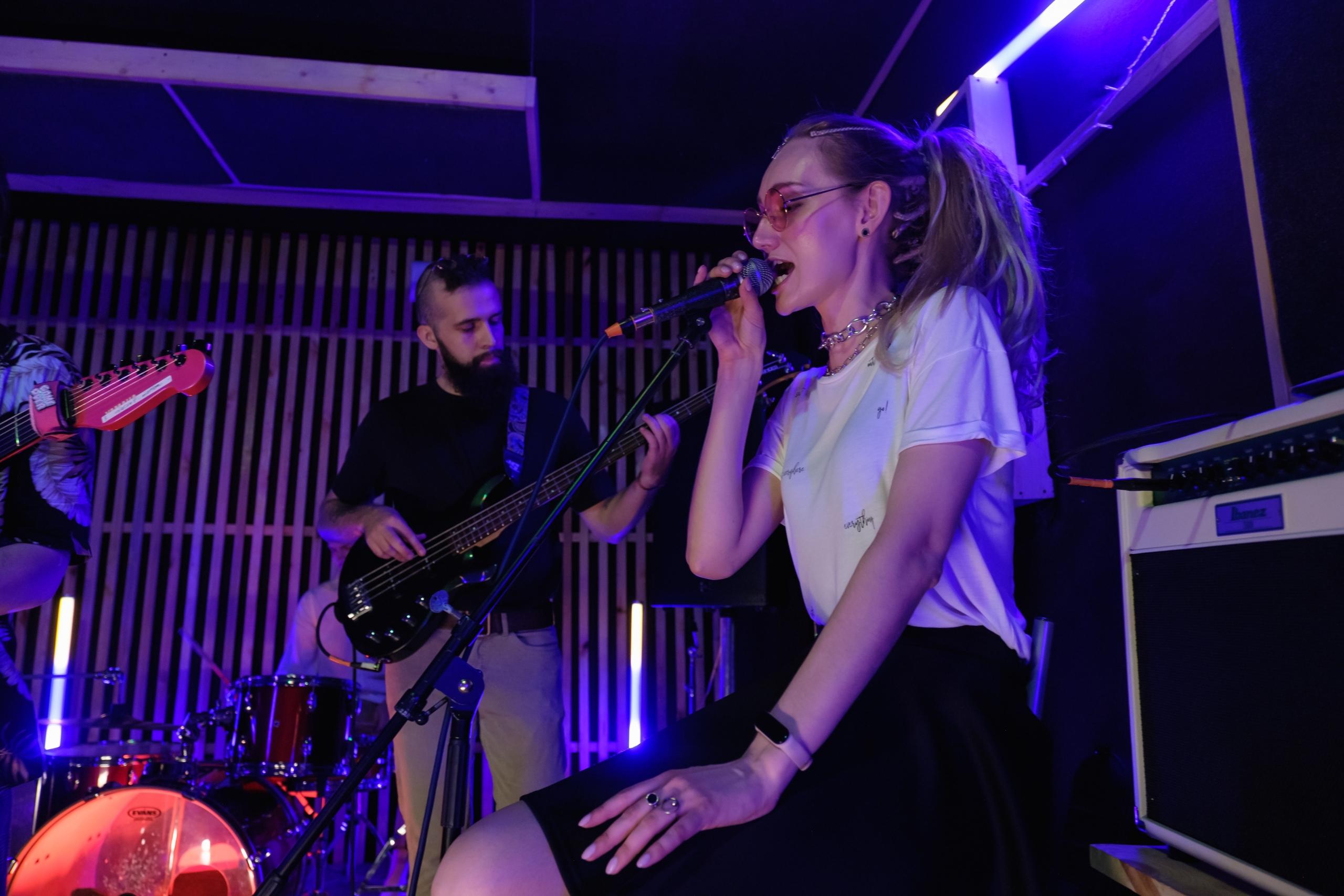 Jente som synger i mikrofon på en scene med et band.