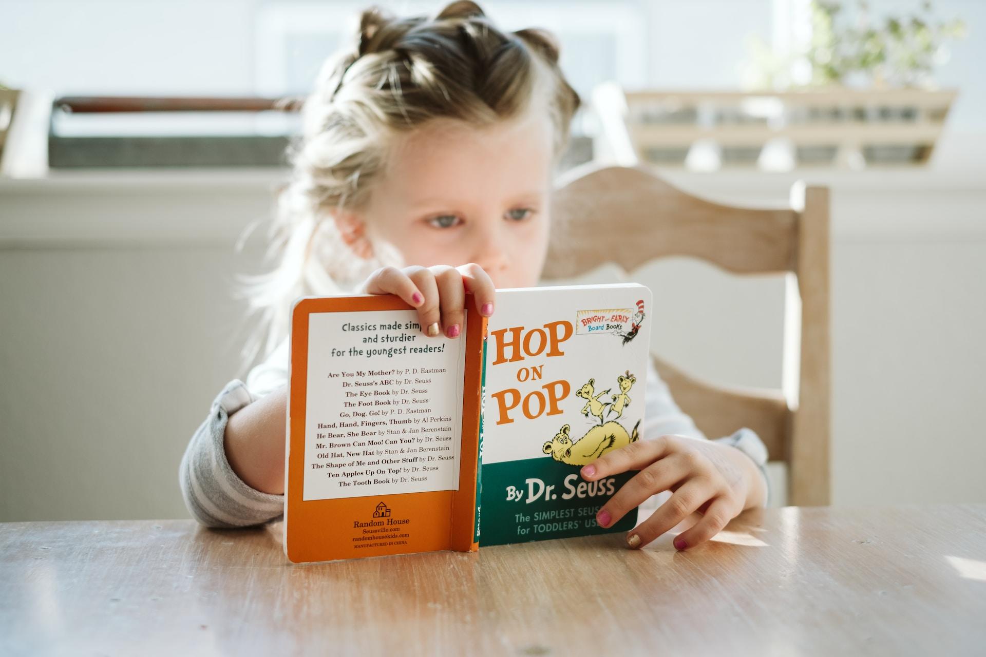 Jente med oppsatt hår leser i en barnebok av Dr.Seuss.