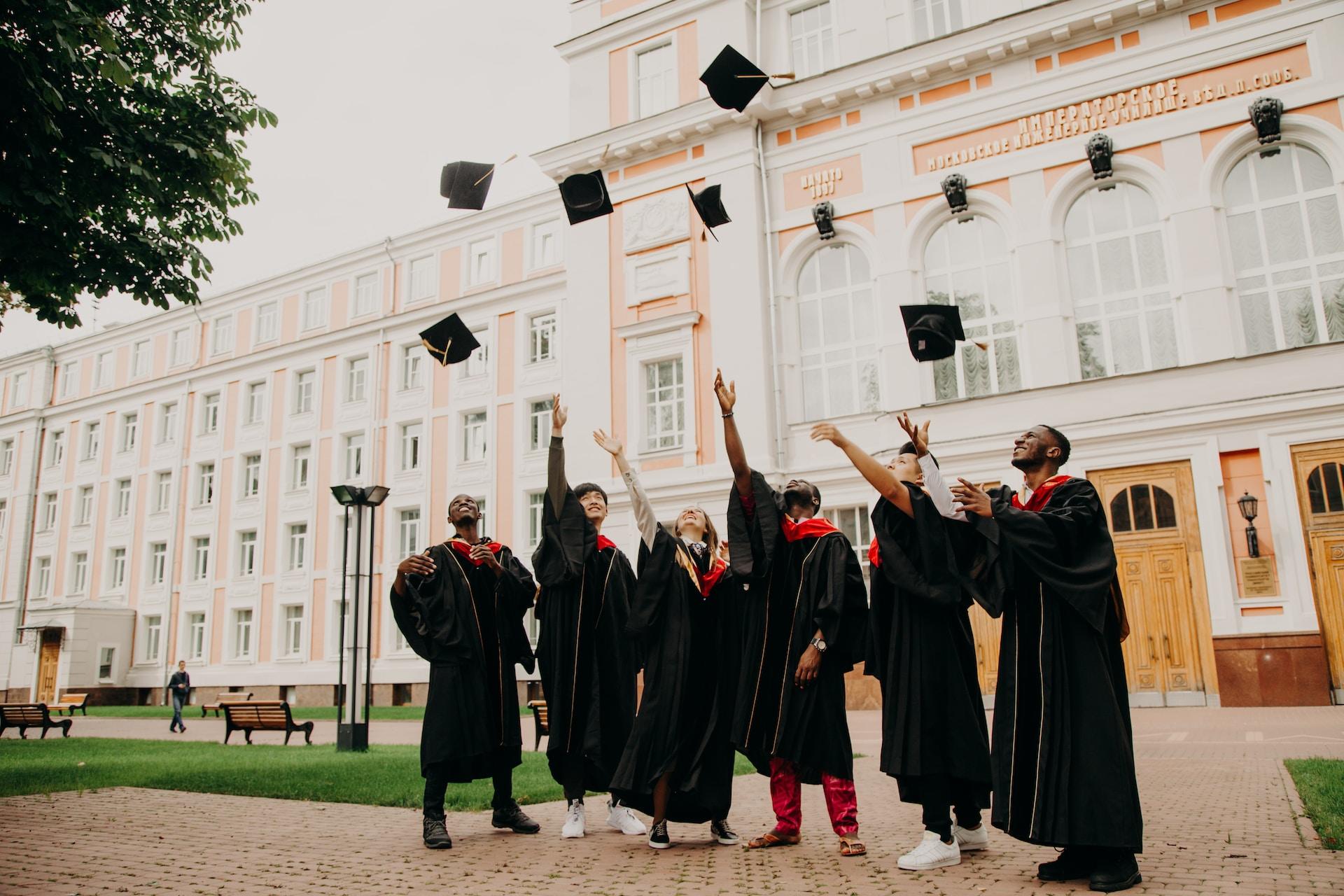 En gruppe med mennesker i kappe kaset hatten sin i været foran universitetet sitt etter utdeling av vitnemål.