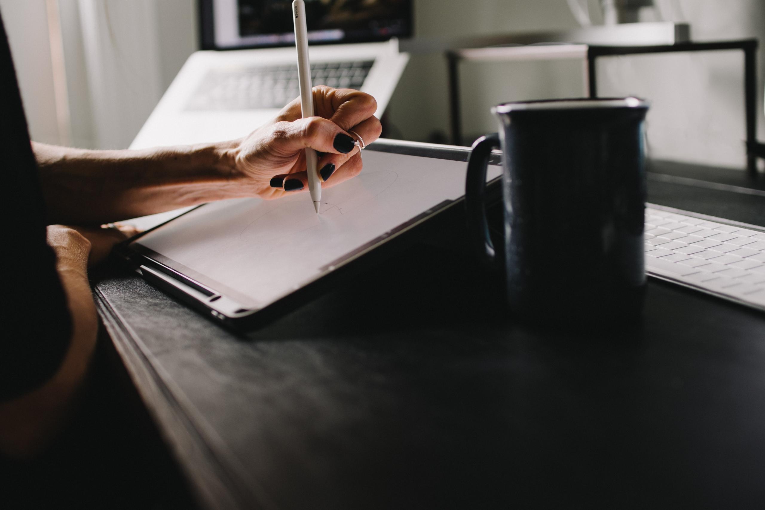 Kvinne skriver med hånd på ipad på lys bakgrunn