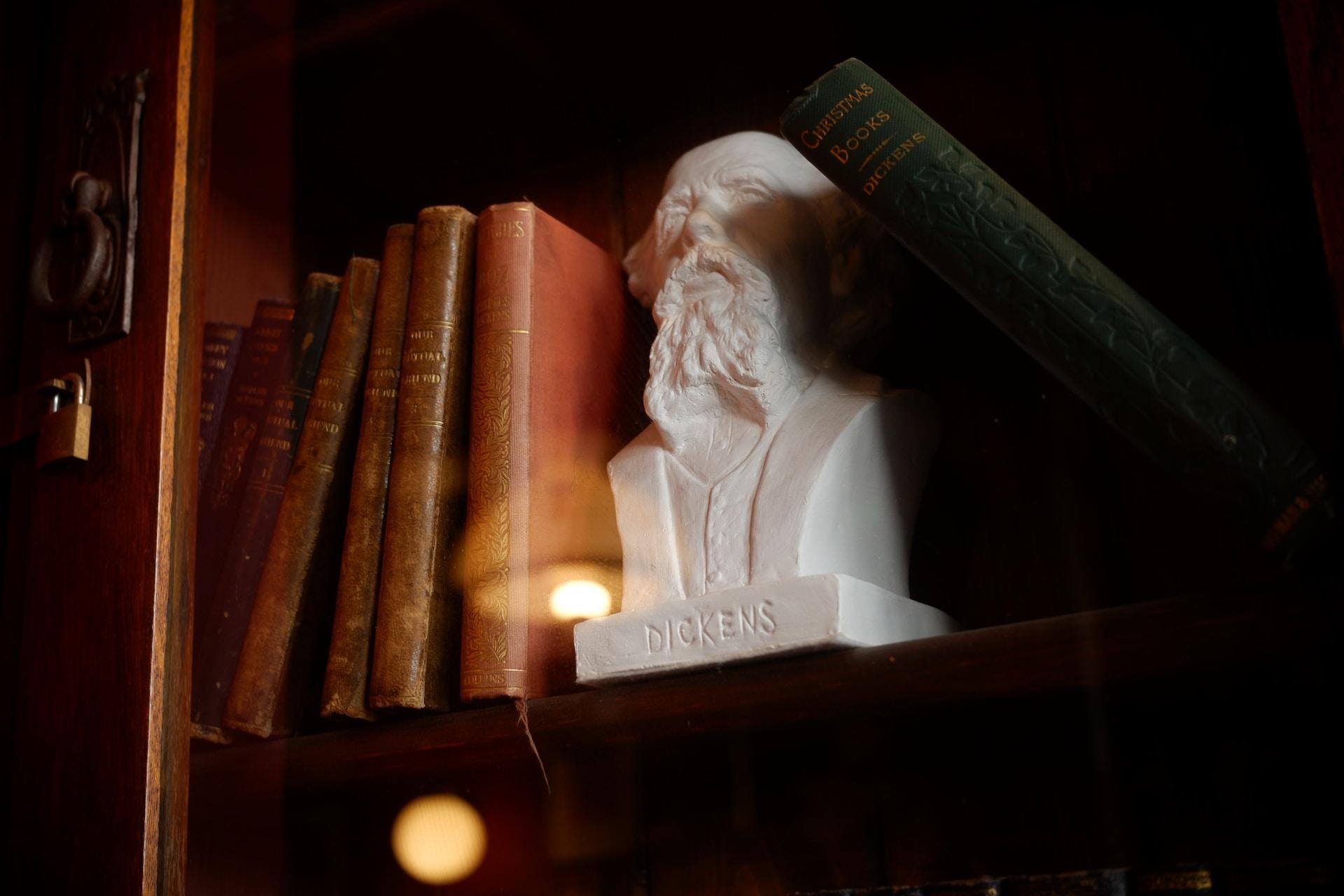 Byste av Charles Dickens mellom bøker i bokhylle.