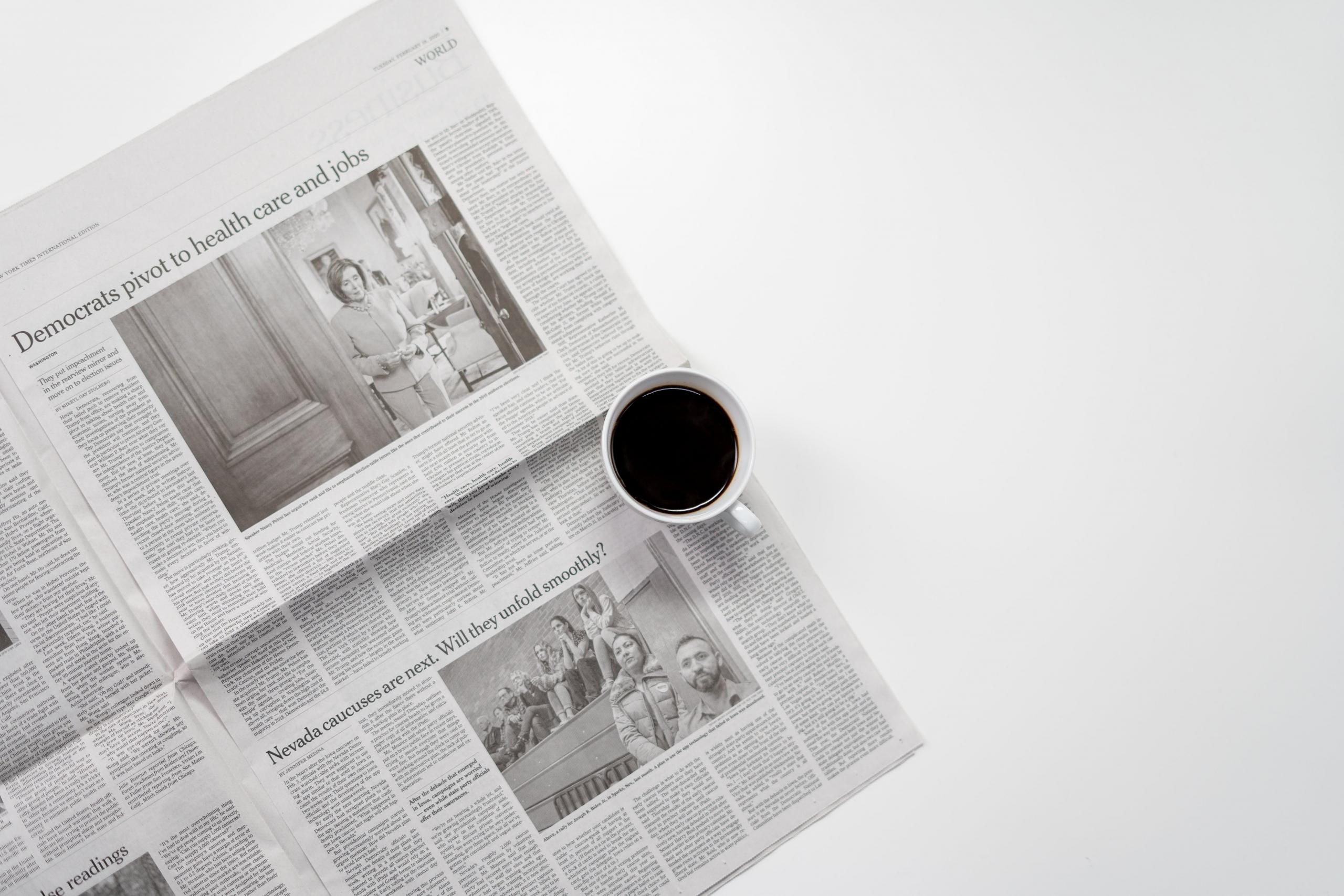 En kaffekopp står plassert oppå en engelskspråklig avis på et hvitt bord