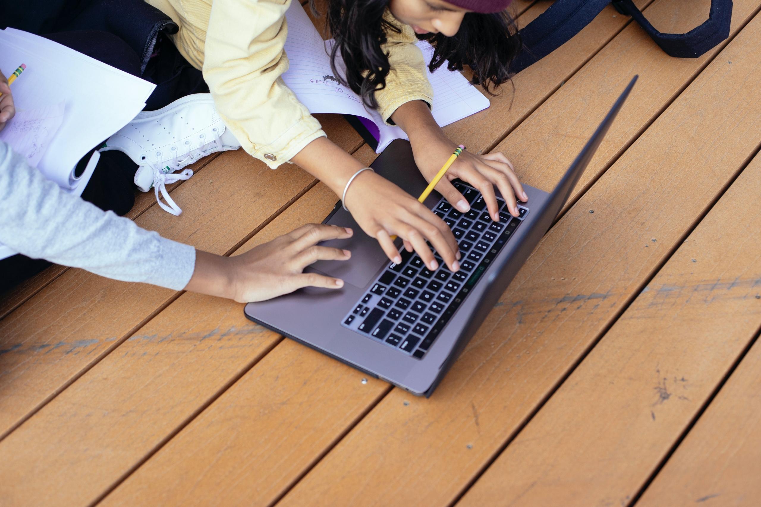 Ivrige studenter trykker på tastaturet til en laptop med tre hender totalt.