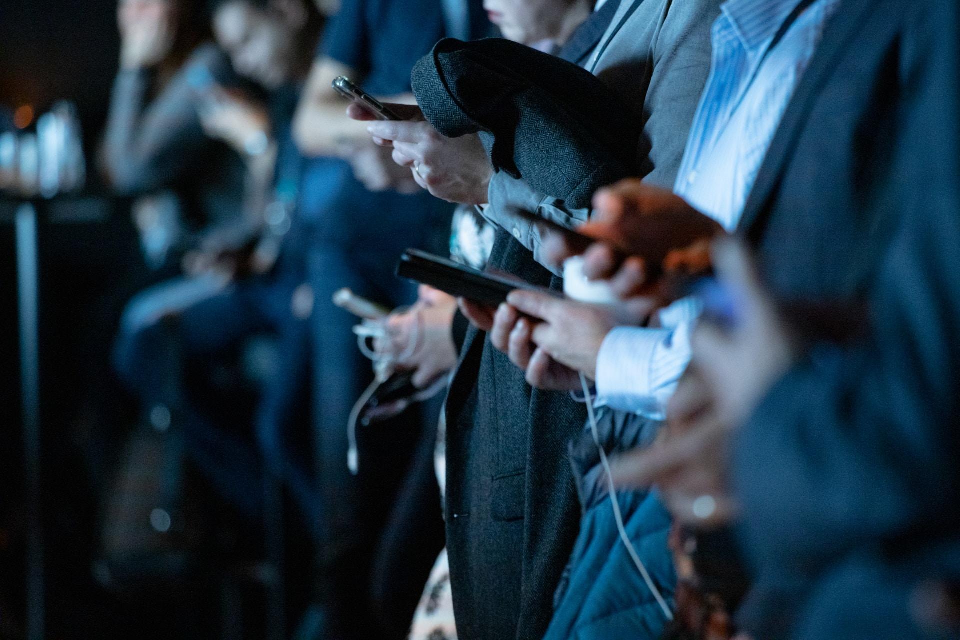 Personer står ved siden av hverandre og ser ned i hver sin telefon.