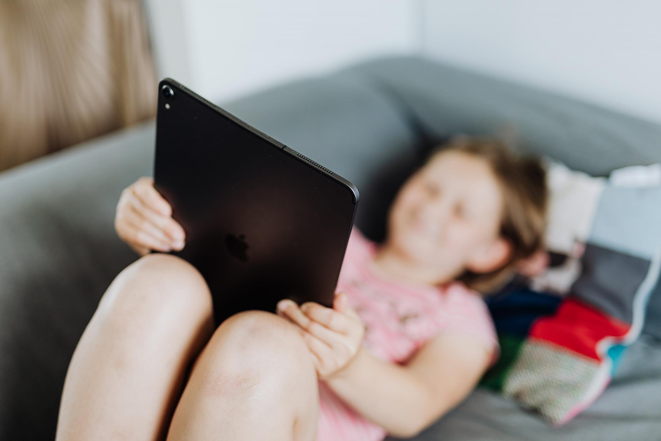 Et barn smilende mens hun holder en iPad, engasjert i et mattespill.