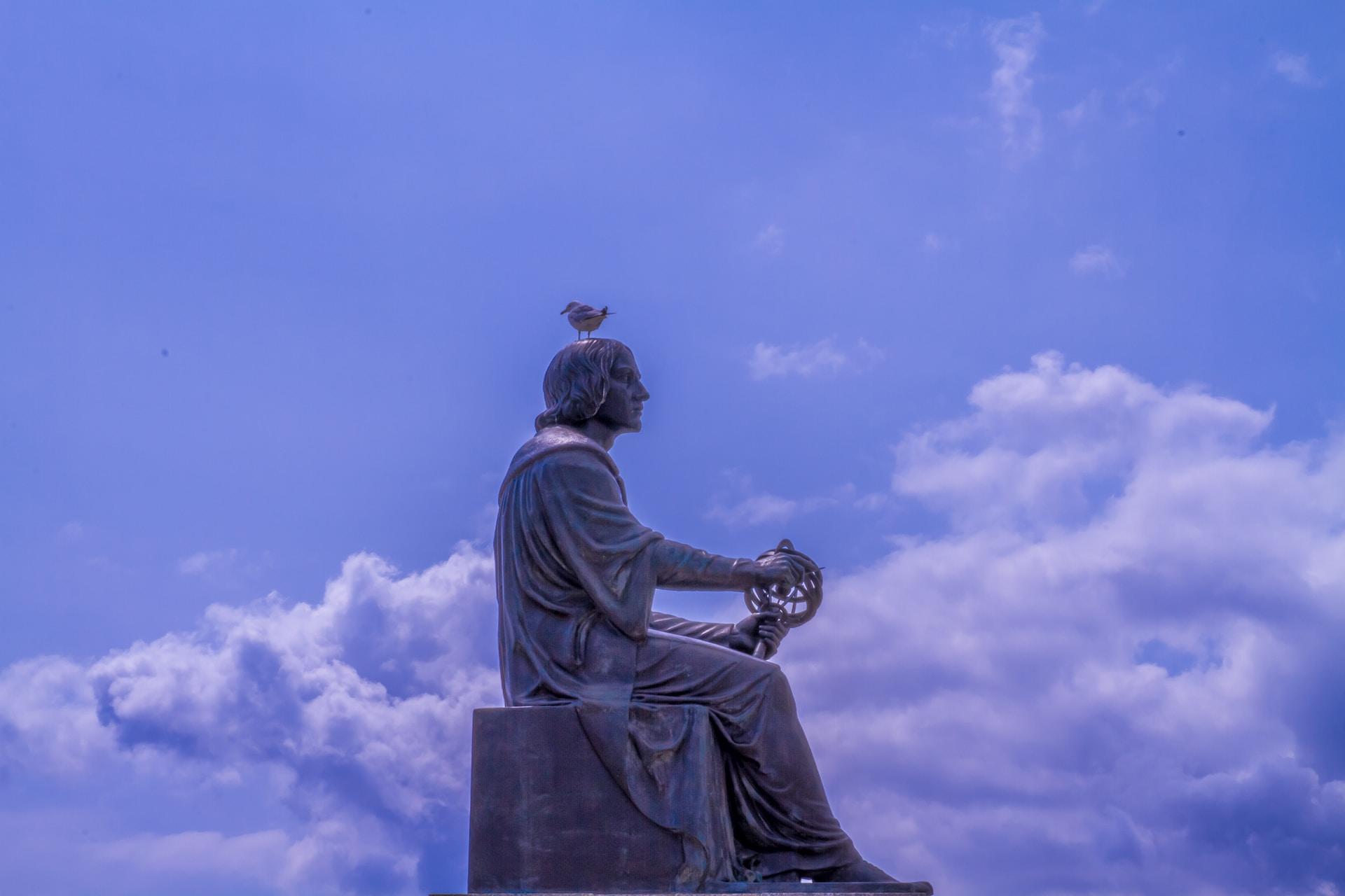 Statue av Copernicus sittende med fugl på hodet.