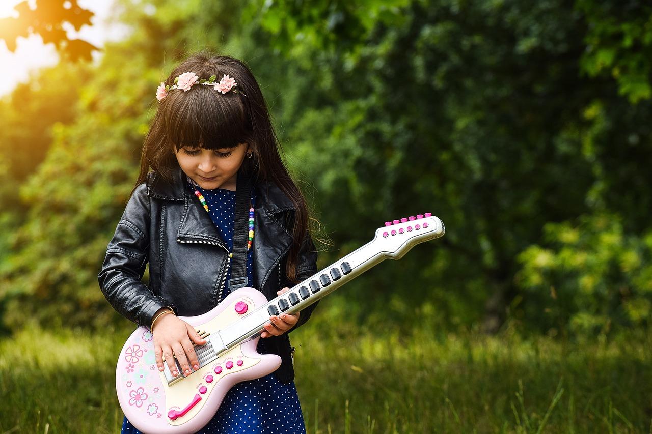 Et barn leker med en rosa lekegitar ute i naturen.