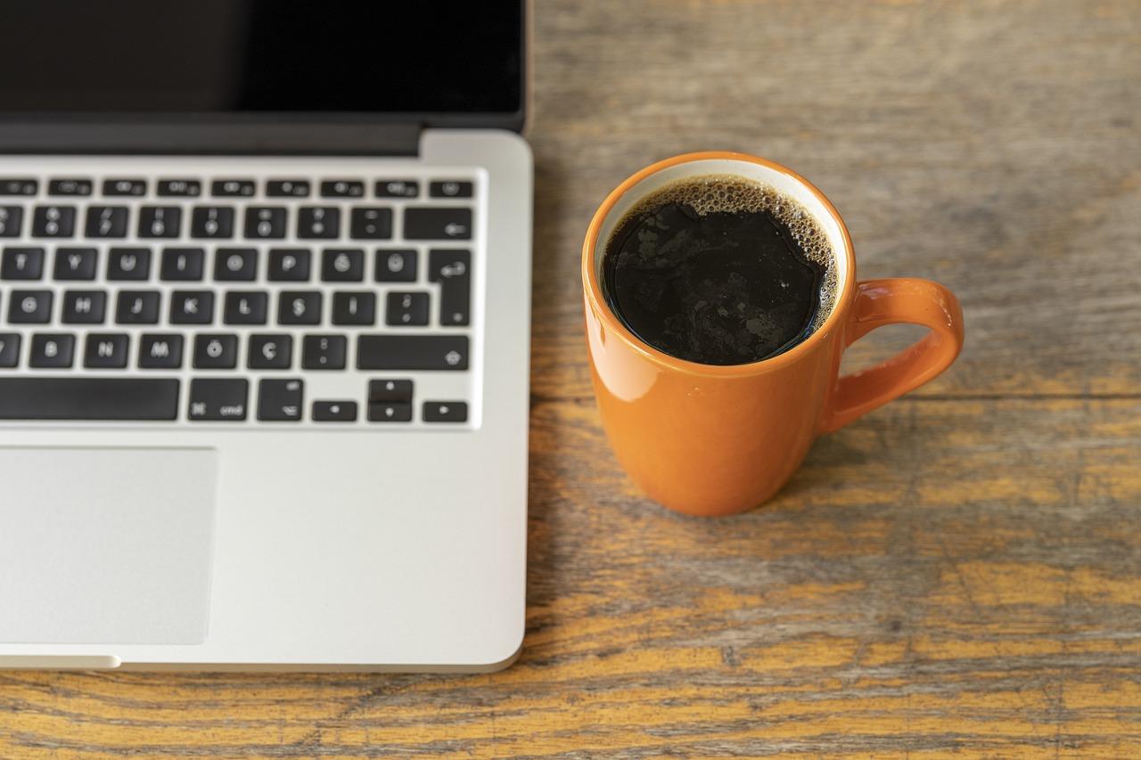 Et åpent bærbart datamaskin og en oransje kaffekopp på et trebord