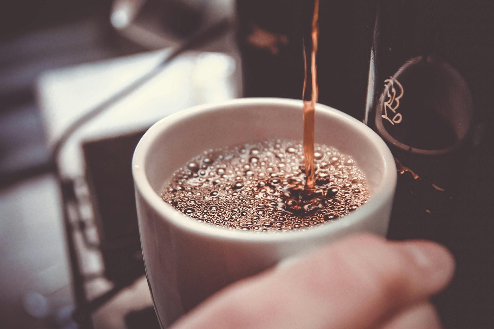Hvit kopp fylles opp med sort kaffe.