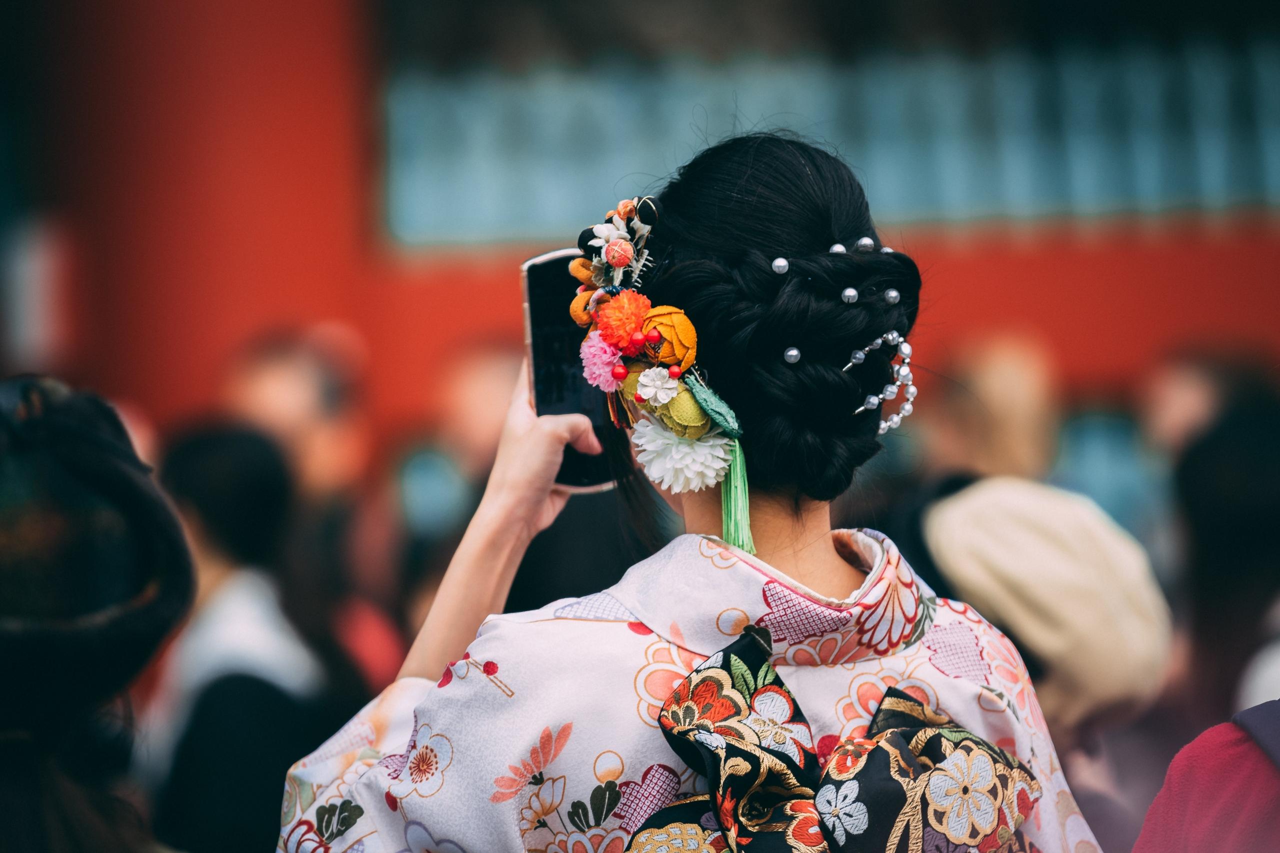 En moderne geisha tar en selfie, med fokus på hennes detaljerte frisyre med fargerike kanzashi og en mønstret kimono.