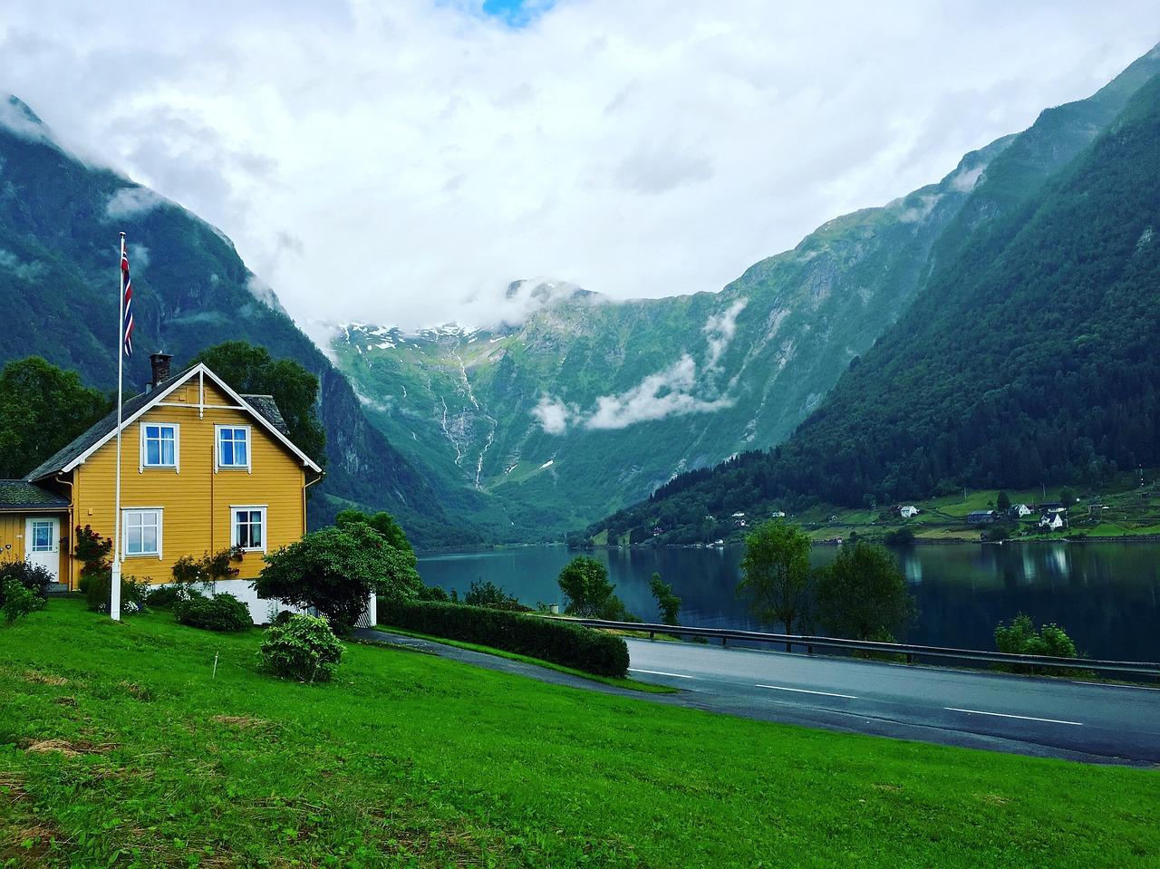 Et tradisjonelt norsk hus foran et fjordlandskap med Norges flagg vaier.