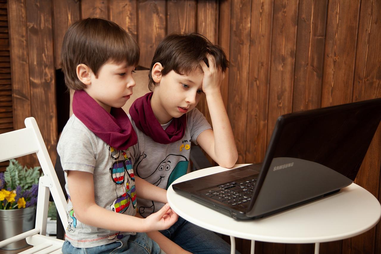 To barn sitter foran en åpen laptop, konsentrert om innholdet mens de tydeligvis forsøker å forstå eller løse et problem.