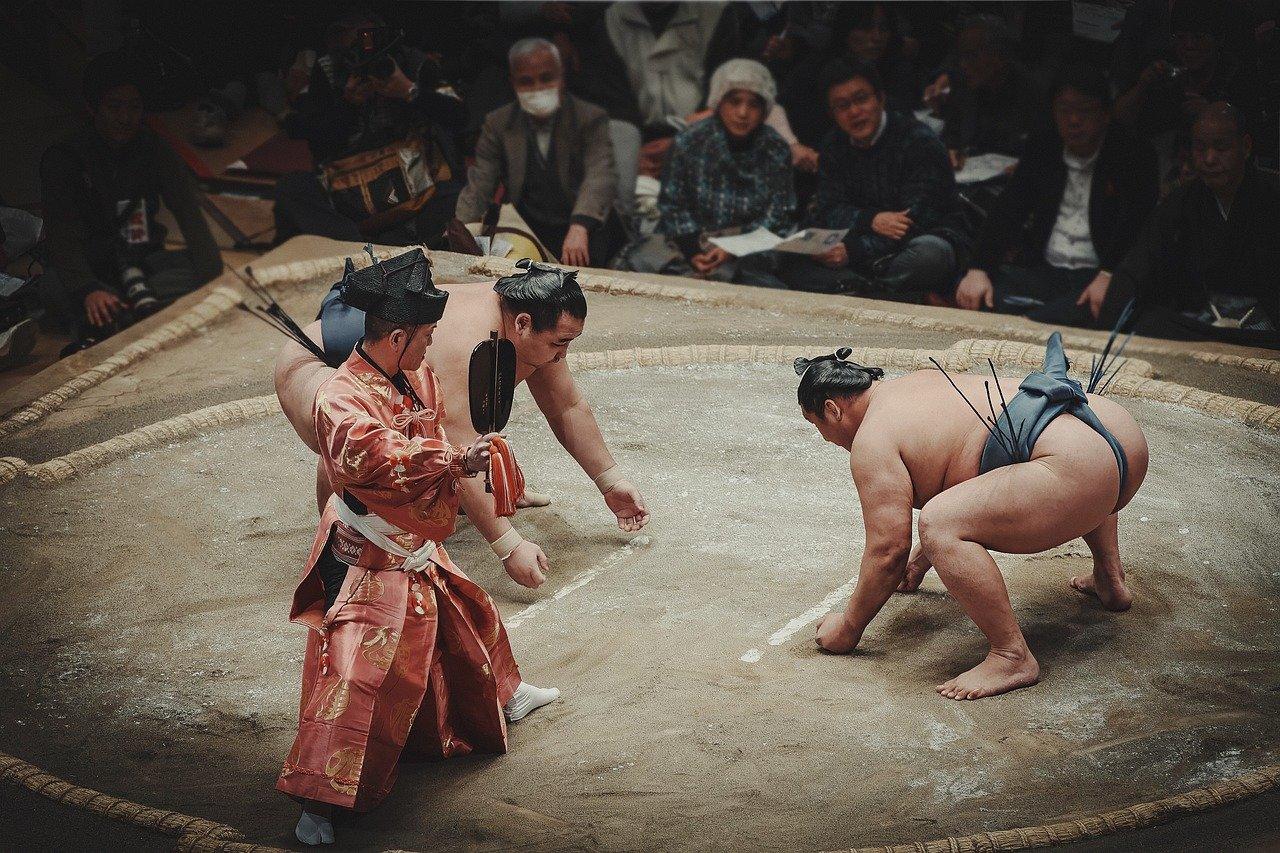 Sumobrytere i en dohyo med en dommer i tradisjonell shinto-klær.