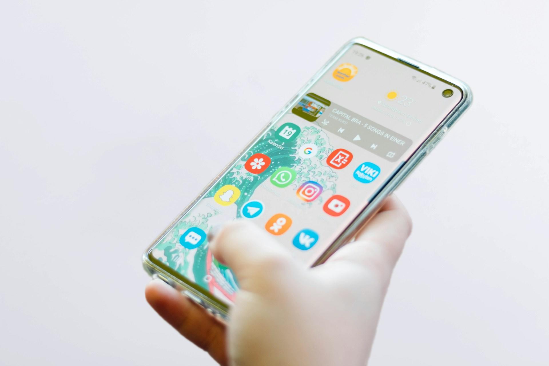 Hånd holder smarttelefon med mange apper på en hjem-skjerm.