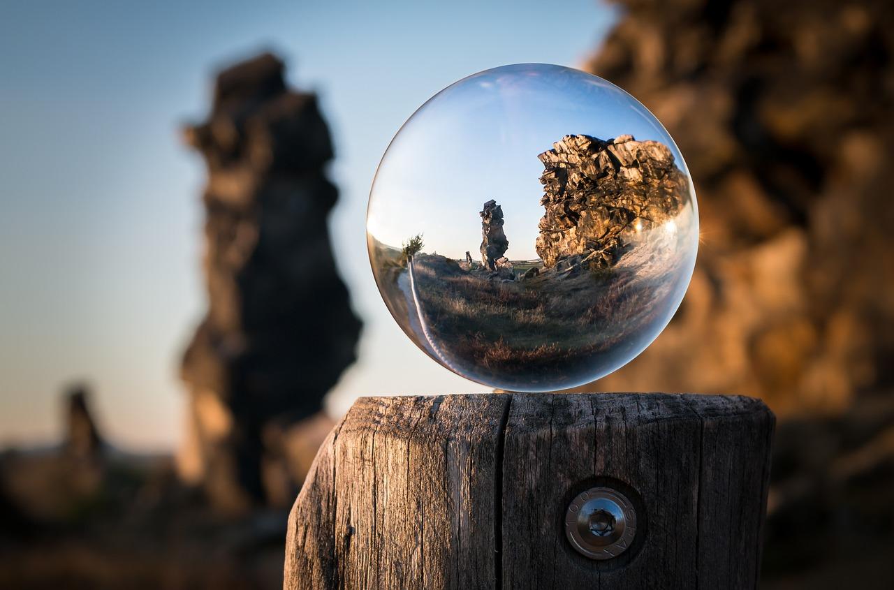 En glasskule plassert på en trestolpe som reflekterer det omkringliggende landskapet med klippeformasjoner.