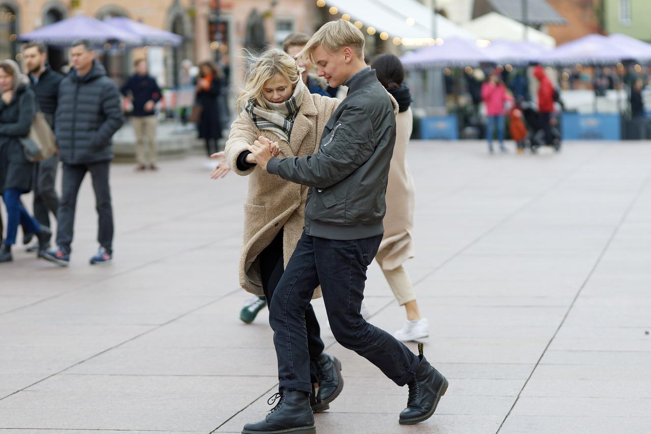 Et ungt par danser vals på et bytorg mens forbipasserende ser på.