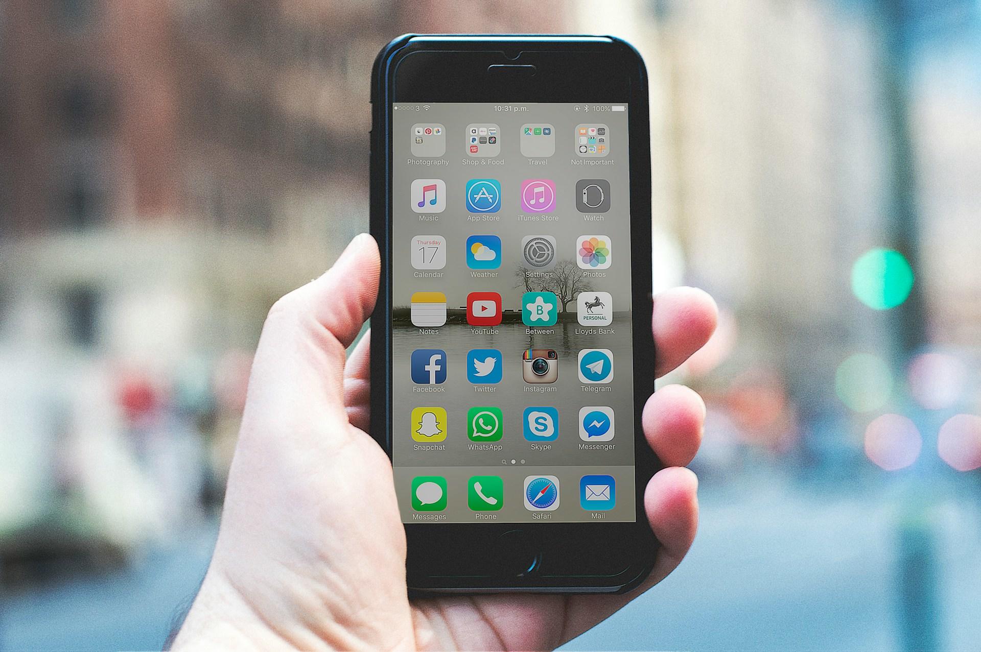 Hånd holder smarttelefon med hjem-skjerm åpen.