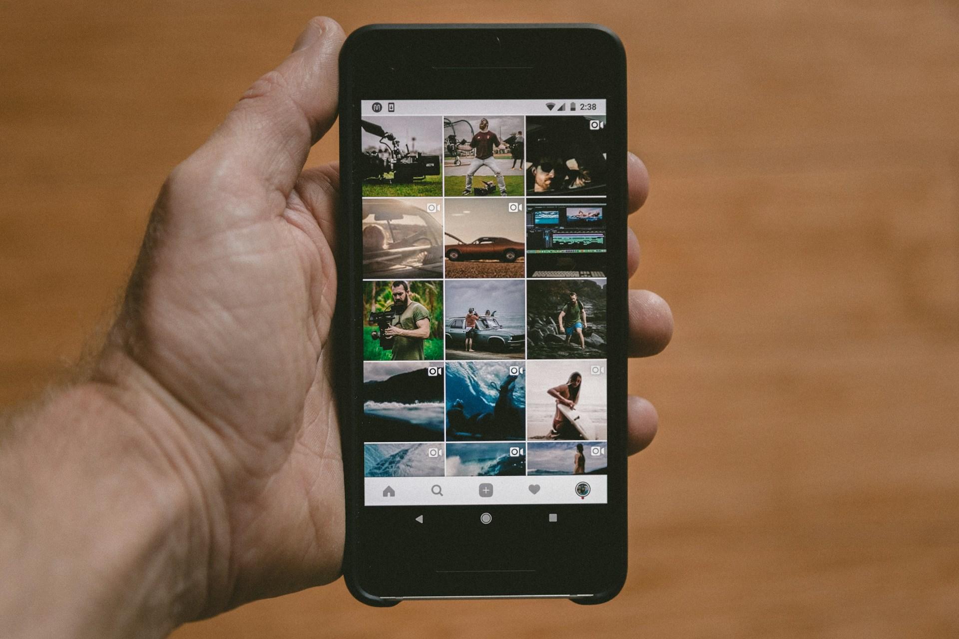 Hånd holder sort mobil med bilder på Instagram.