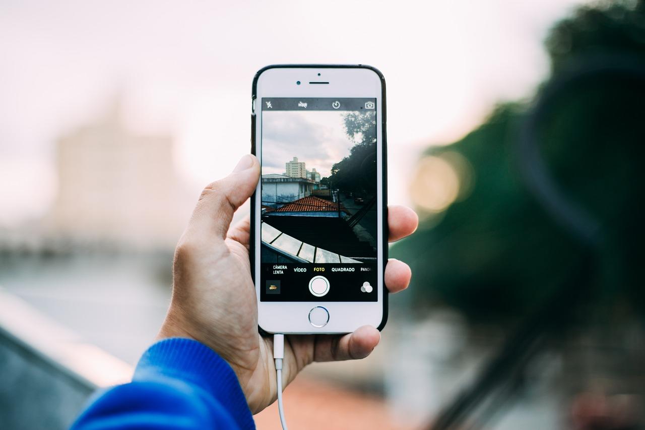 Hånd som holder en iPhone med kamera-app åpen, klar til å ta bilde av et bylandskap.