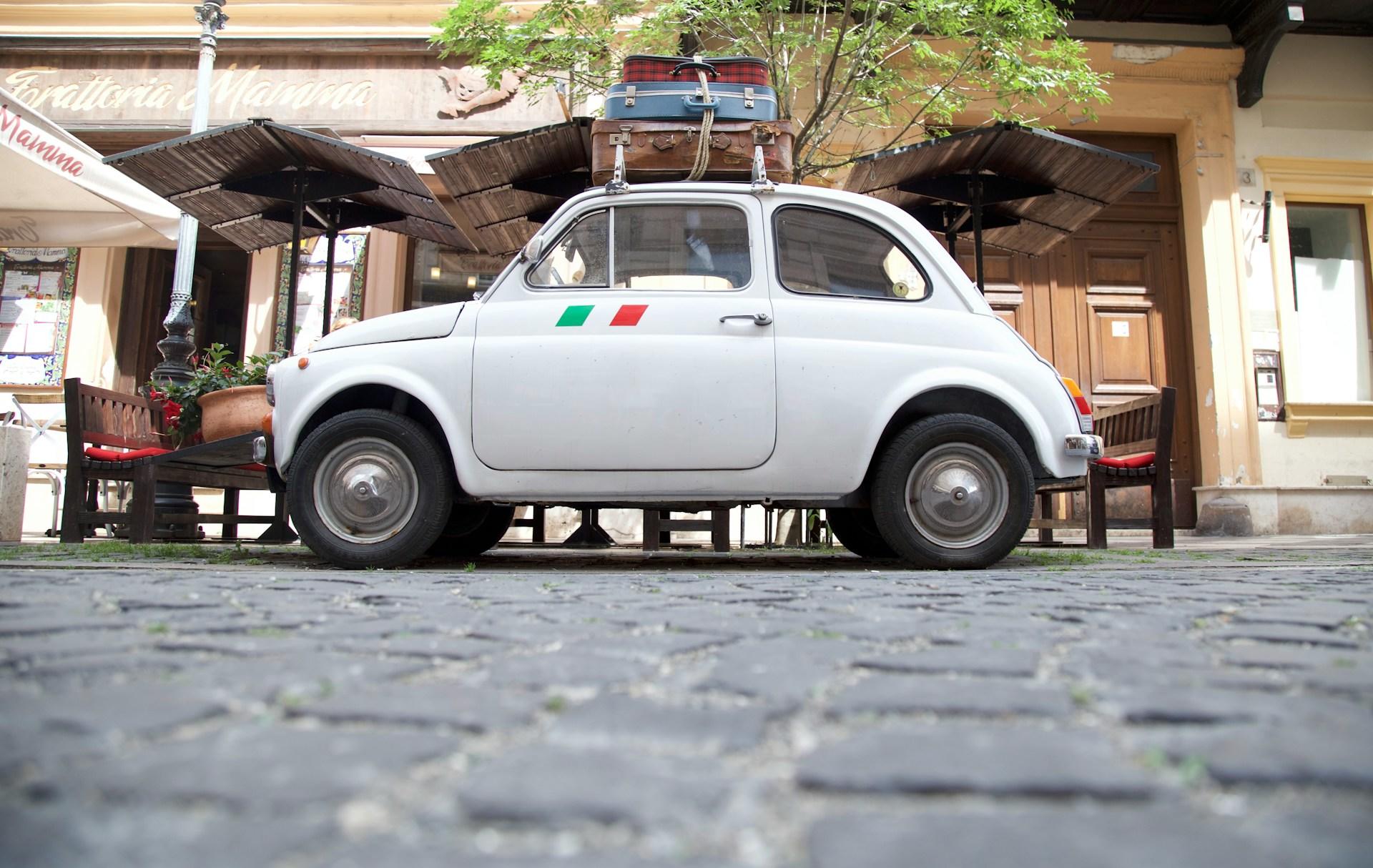 Hvit fiat med koffert på taket og italiensk flagg.
