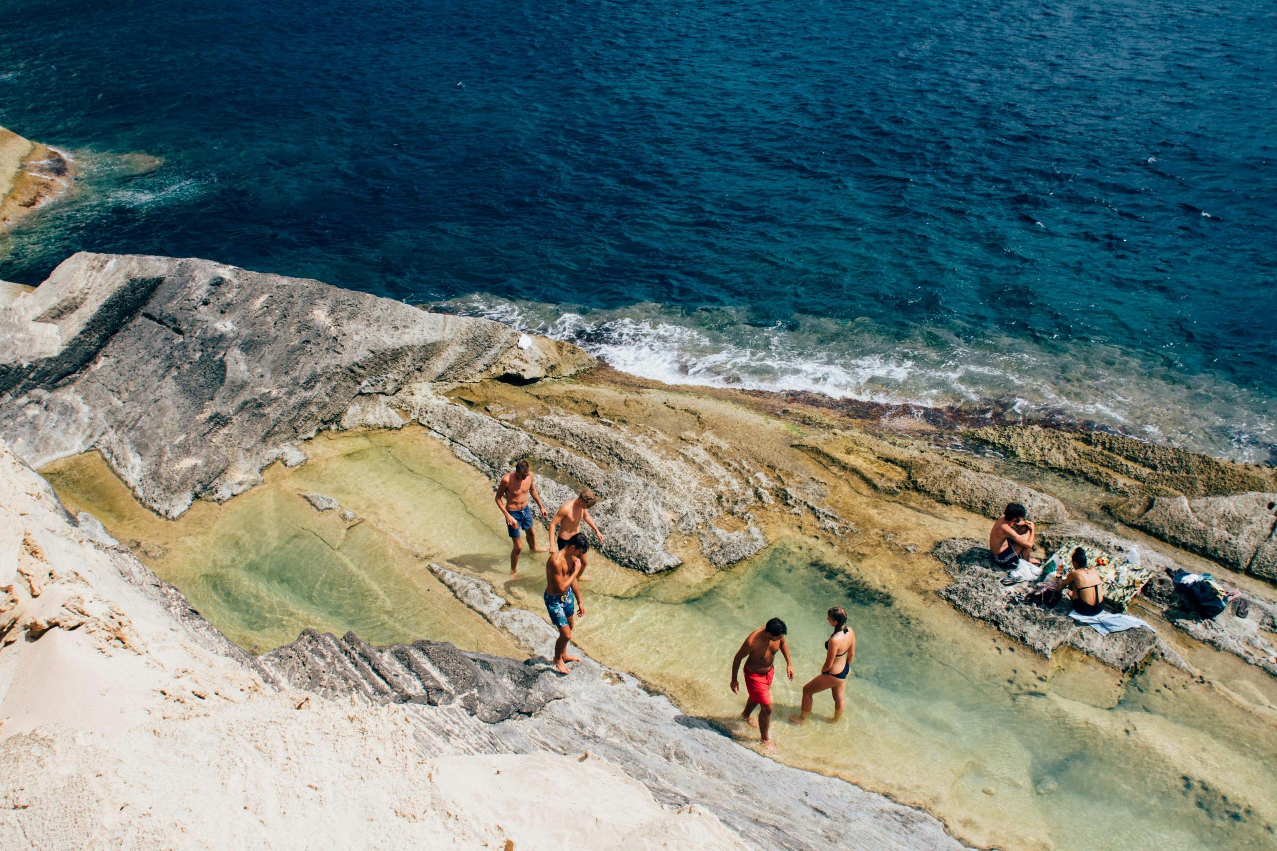 Folk slapper av i naturlige steinbassenger ved kysten av Ibiza.