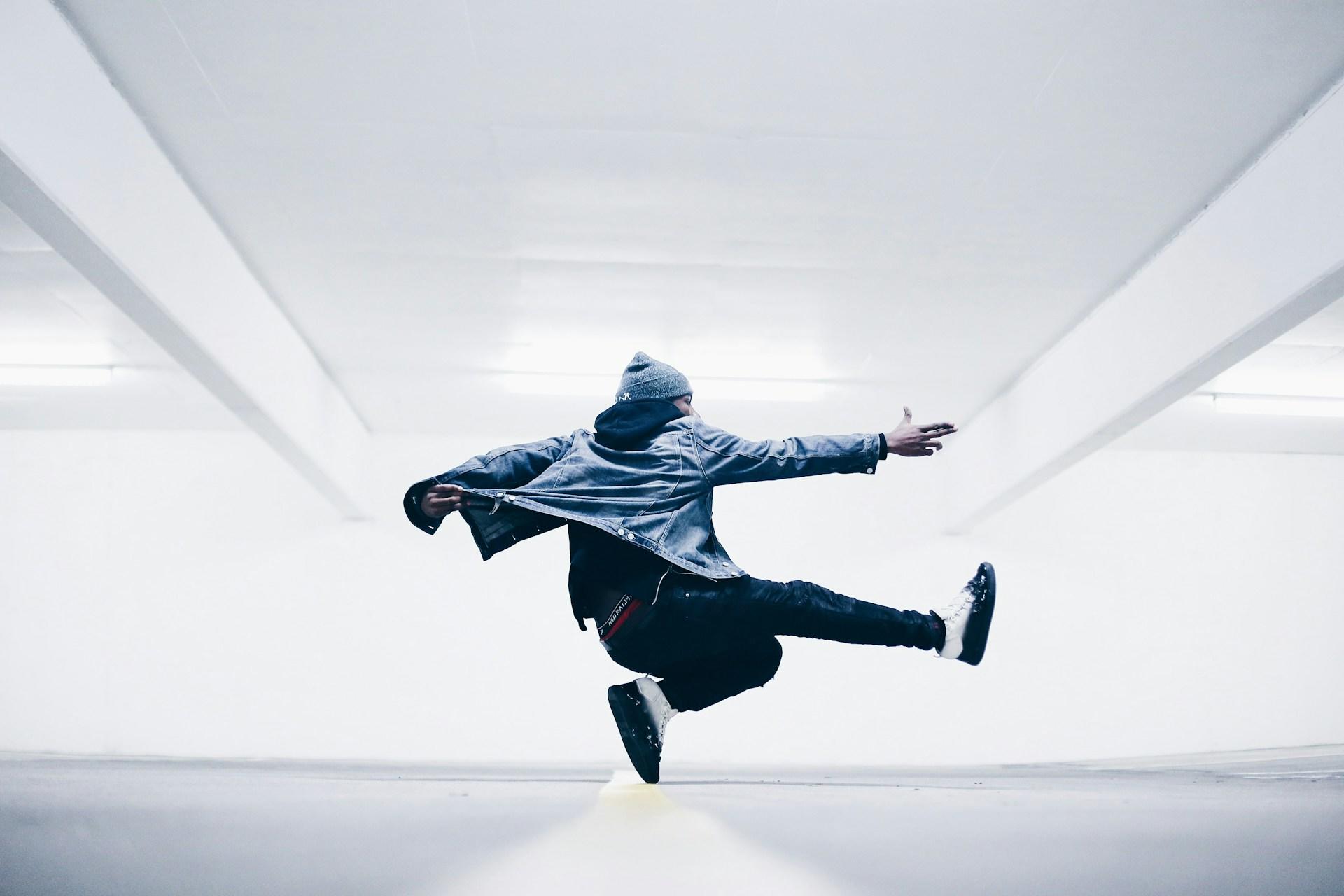 Mann med lue danser i et tomt hvitt rom.