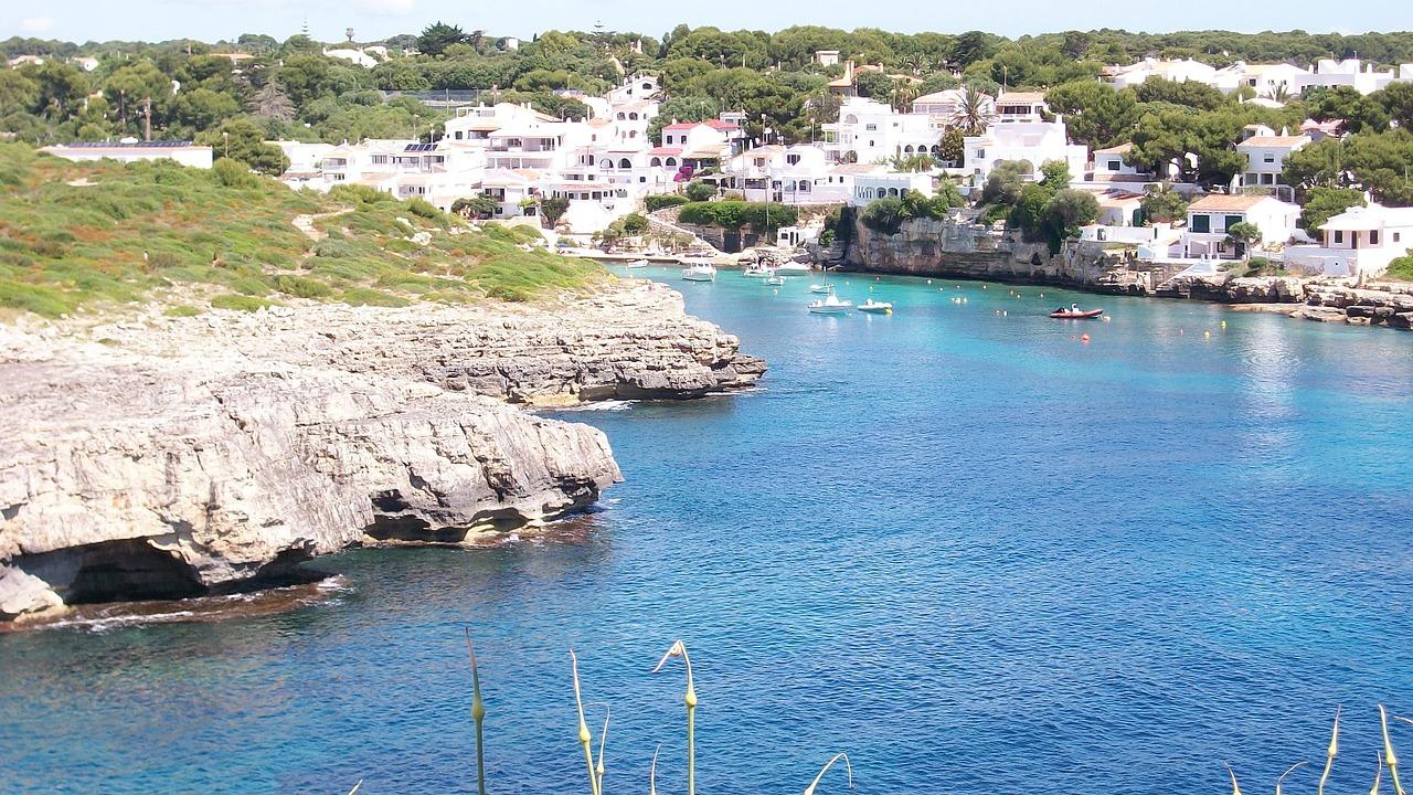 Hvitkalkede hus langs en klippekyst med klart blått vann i Menorca.