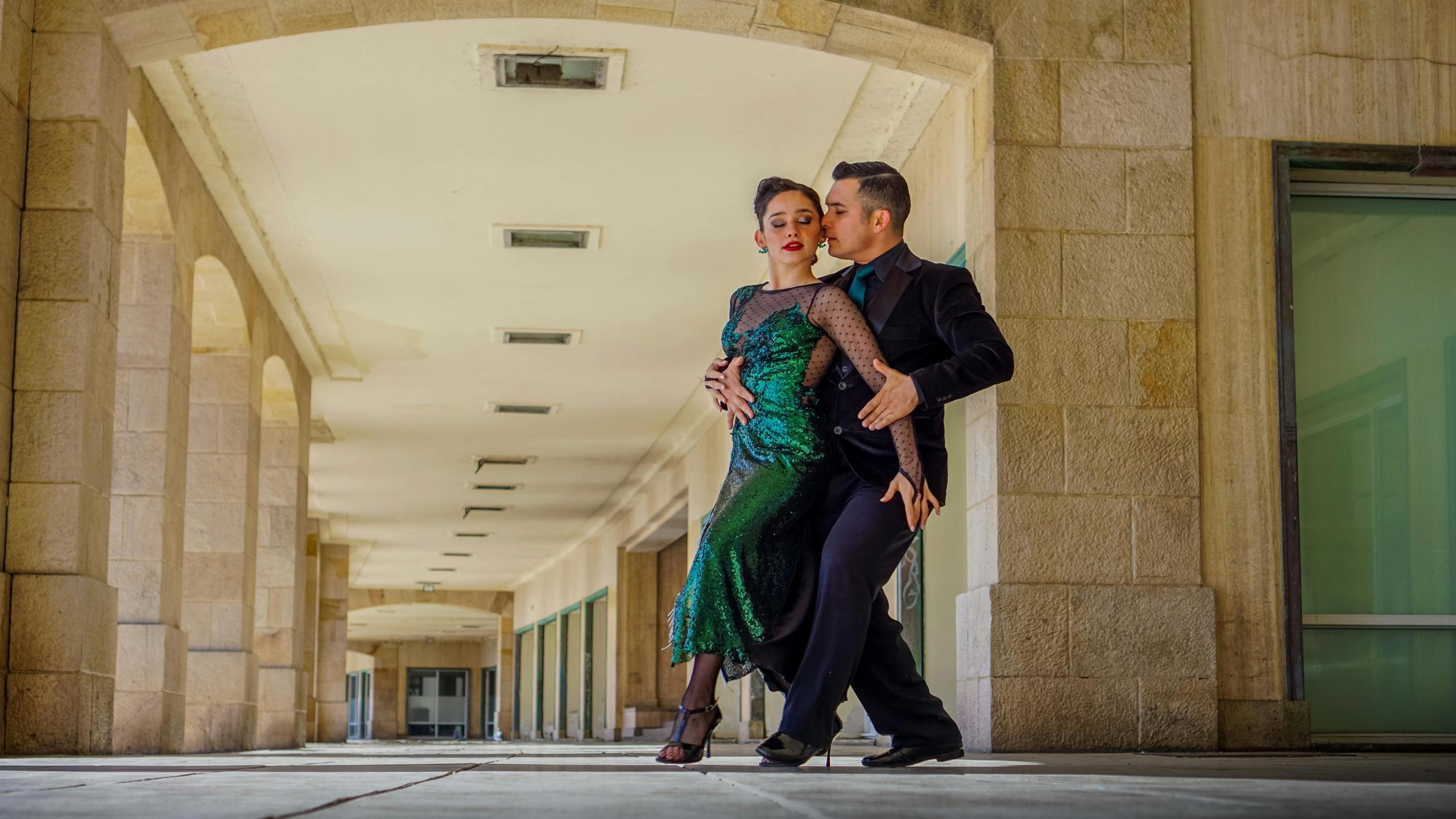 Et par danser tango på en åpen arkade, kledd i formelle danseklær, med en intens og følelsesladet posisjon.