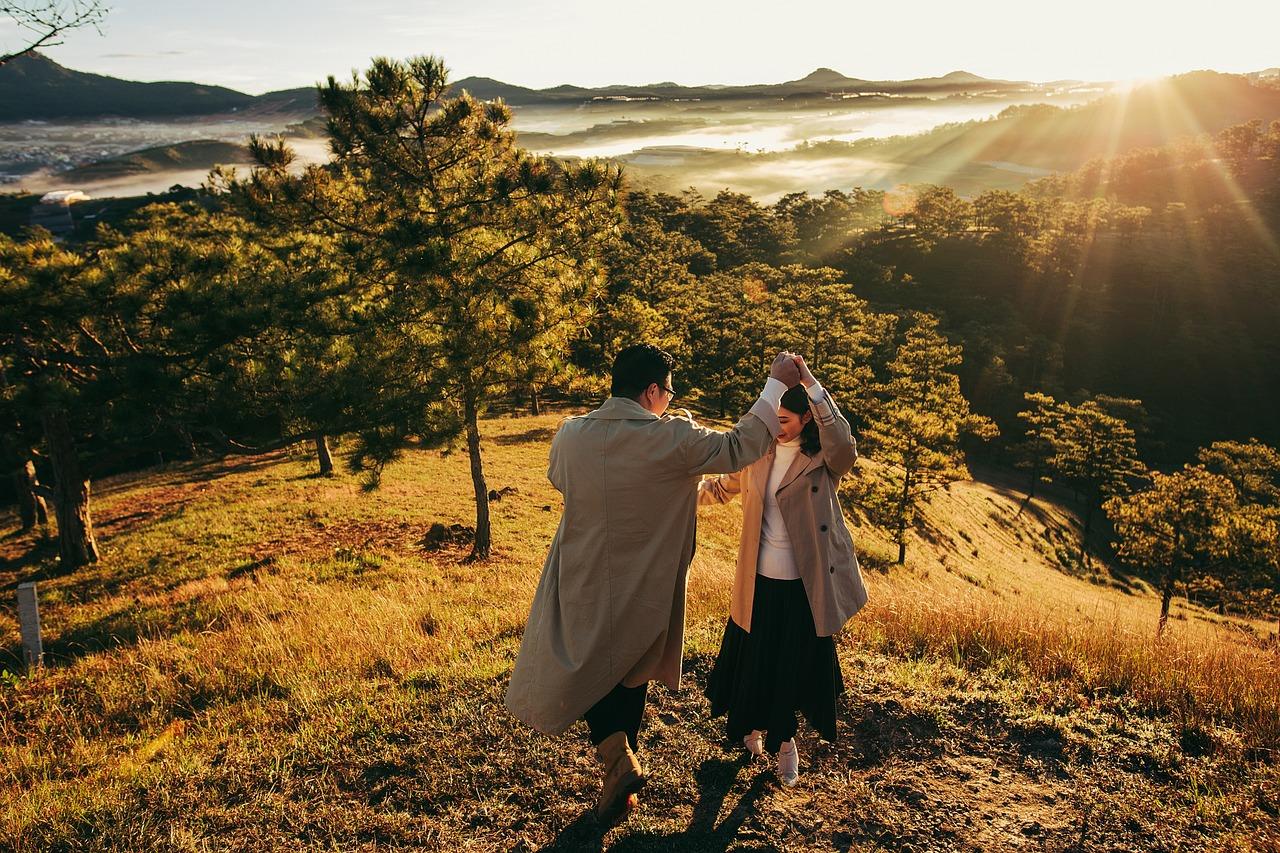 Et par danser på en åsside ved soloppgang, med utsikt over et tåkelagt landskap.