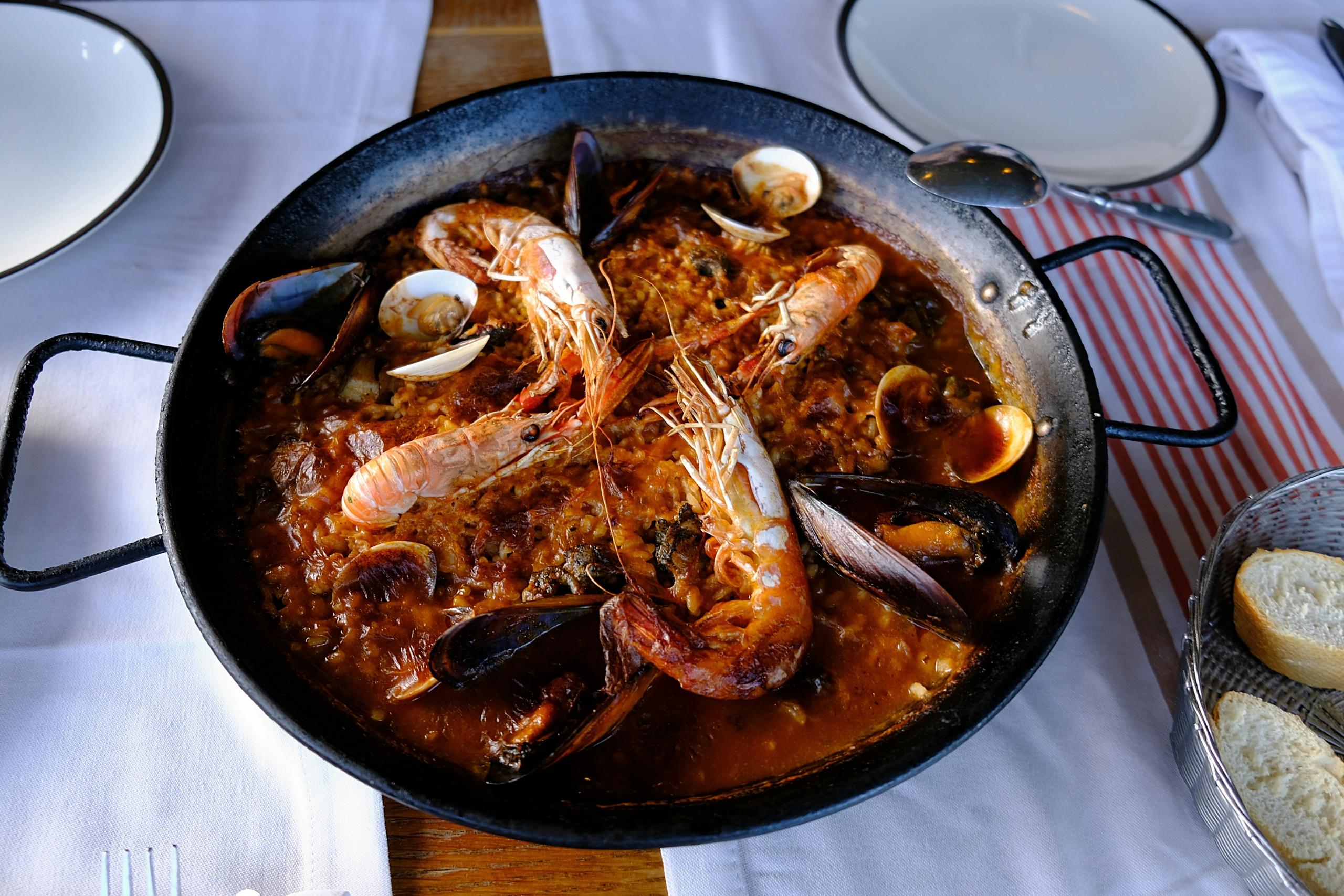Et bord med hvit duk og talerkner med en panne med paella. 