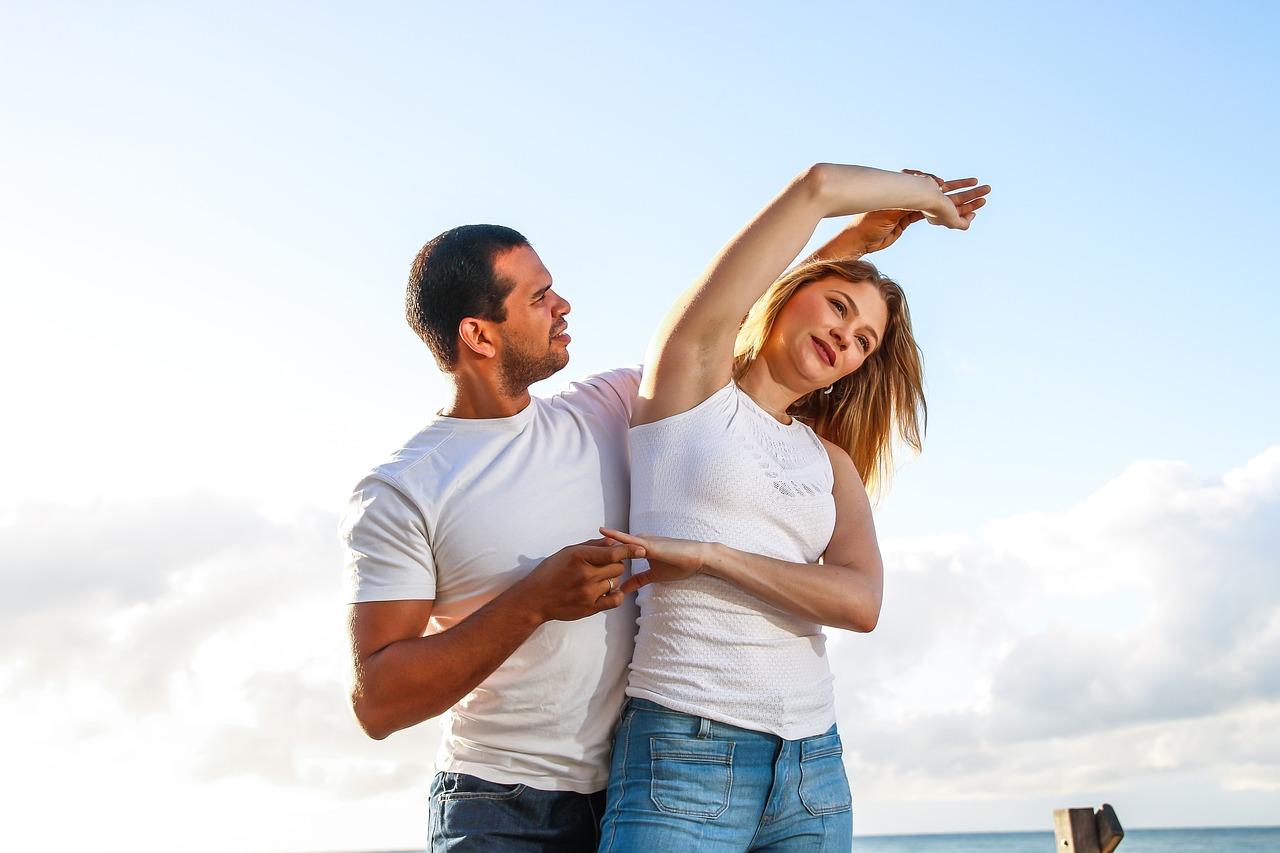 Et par danser sammen på stranden, med armen løftet i en dansestilling.