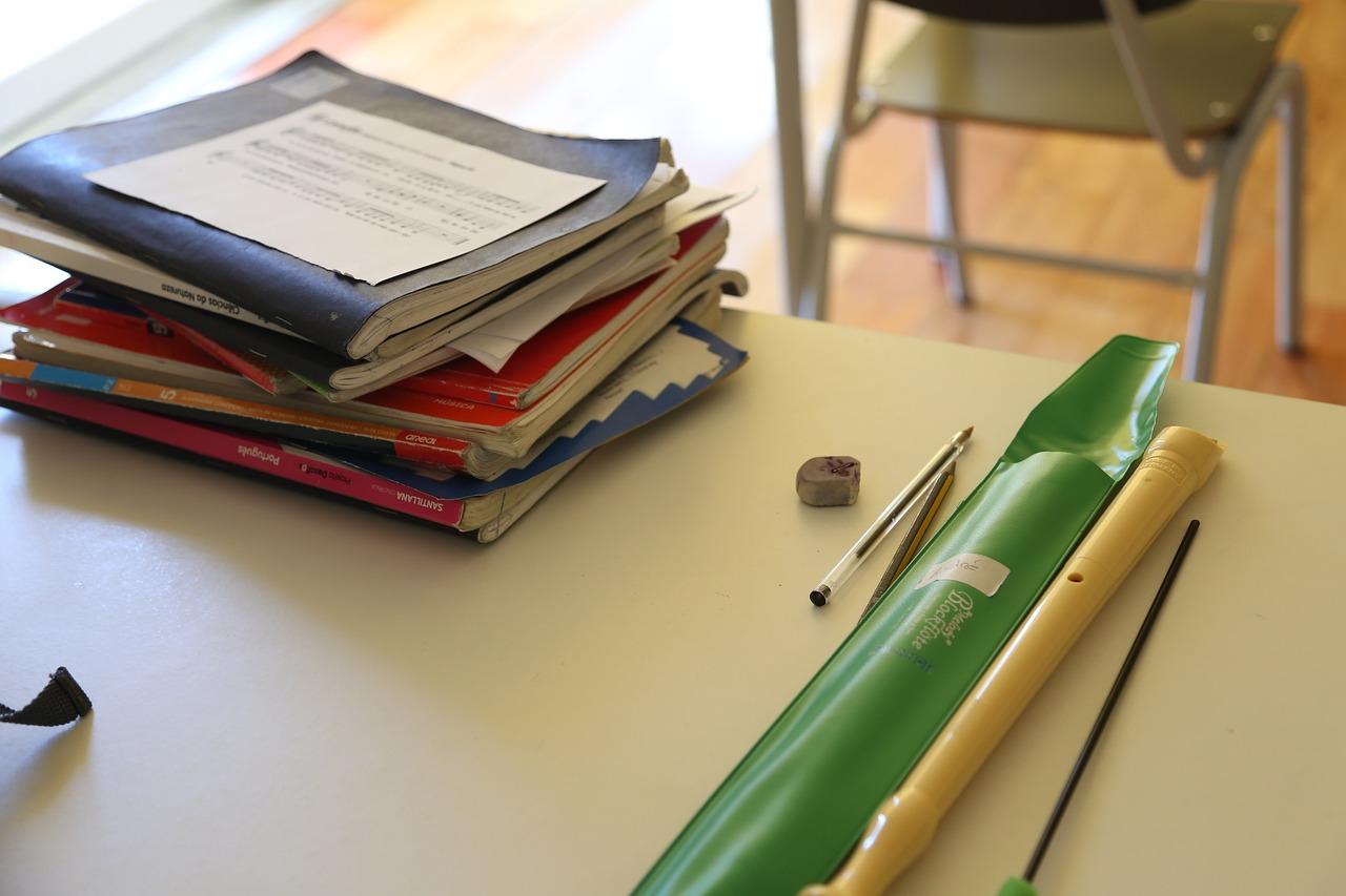 Et skolepult med en bunke noteark, en blokkfløyte og andre skolemateriell.