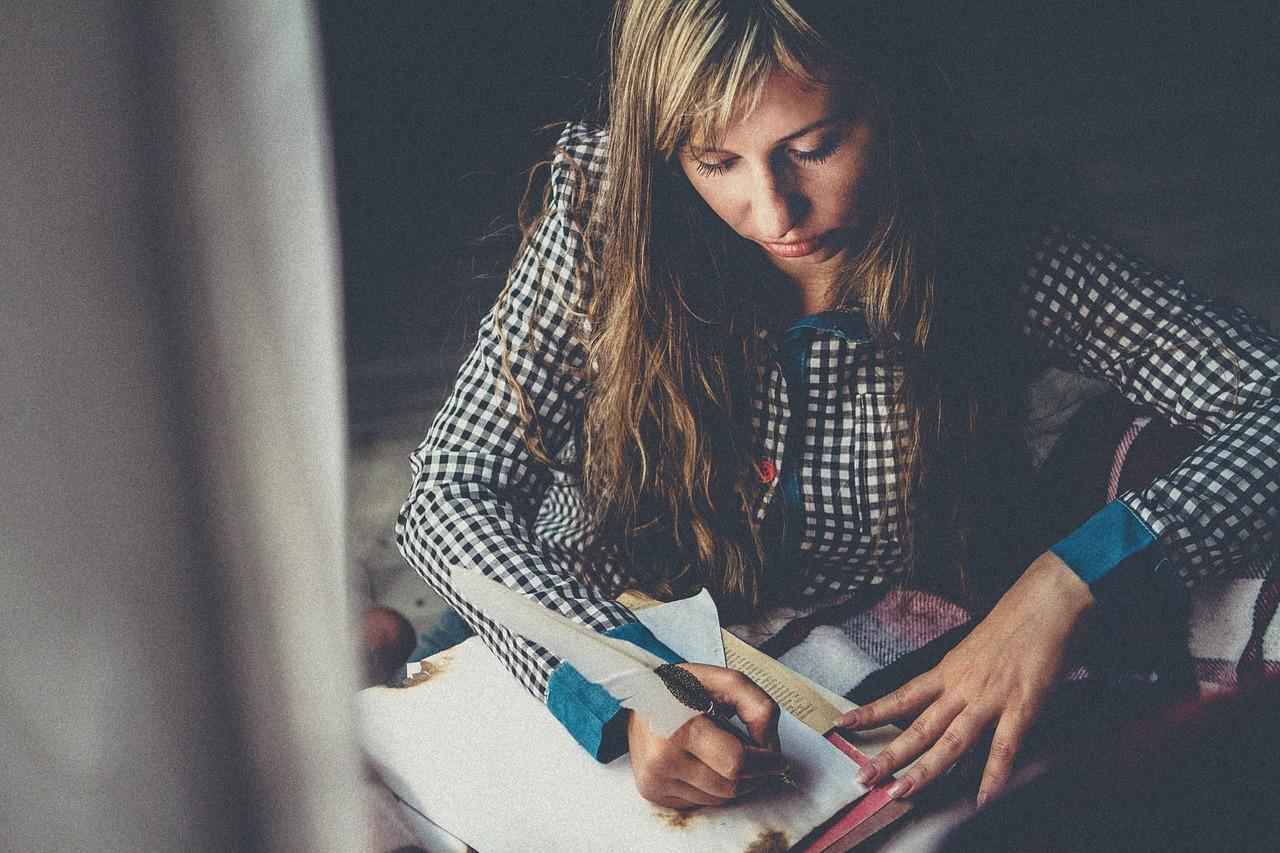 Kvinne i rutete skjorte sitter og skriver intenst i en notatbok.