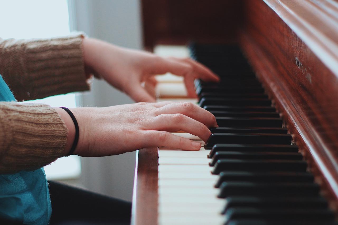 Barnehender spiller varsomt på tangentene til et brunt piano.