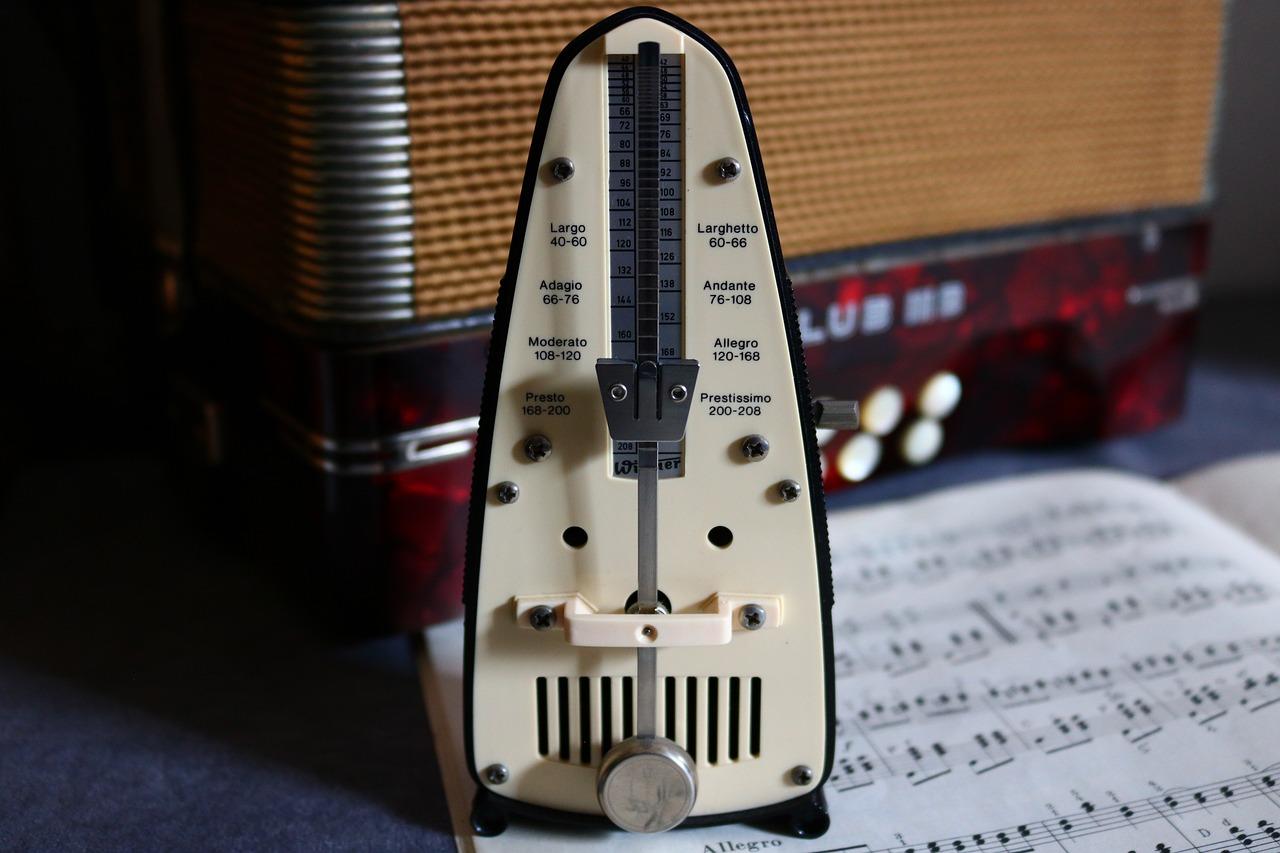 En metronom i forgrunnen med en noteblokk og en gitarforsterker i bakgrunnen.