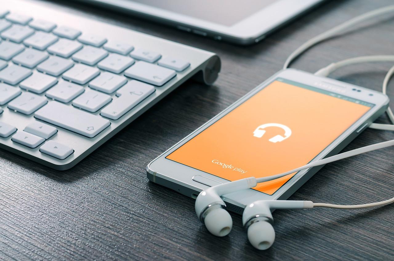 En smarttelefon koblet til øretelefoner ved siden av et tastatur og nettbrett, klar for musikkproduksjon.