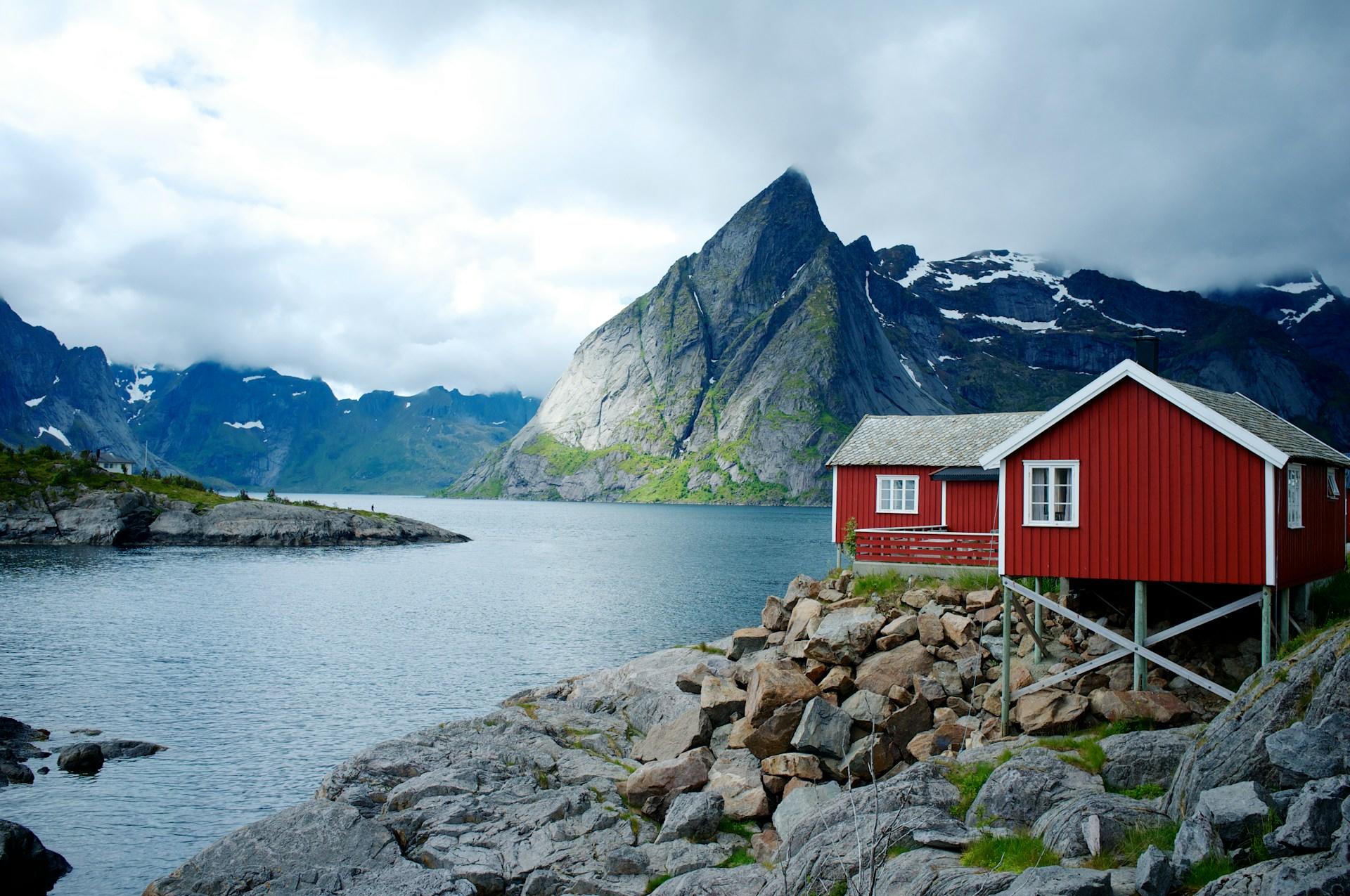 Rødt hus ved fjorden og fjell i bakgrunnen.