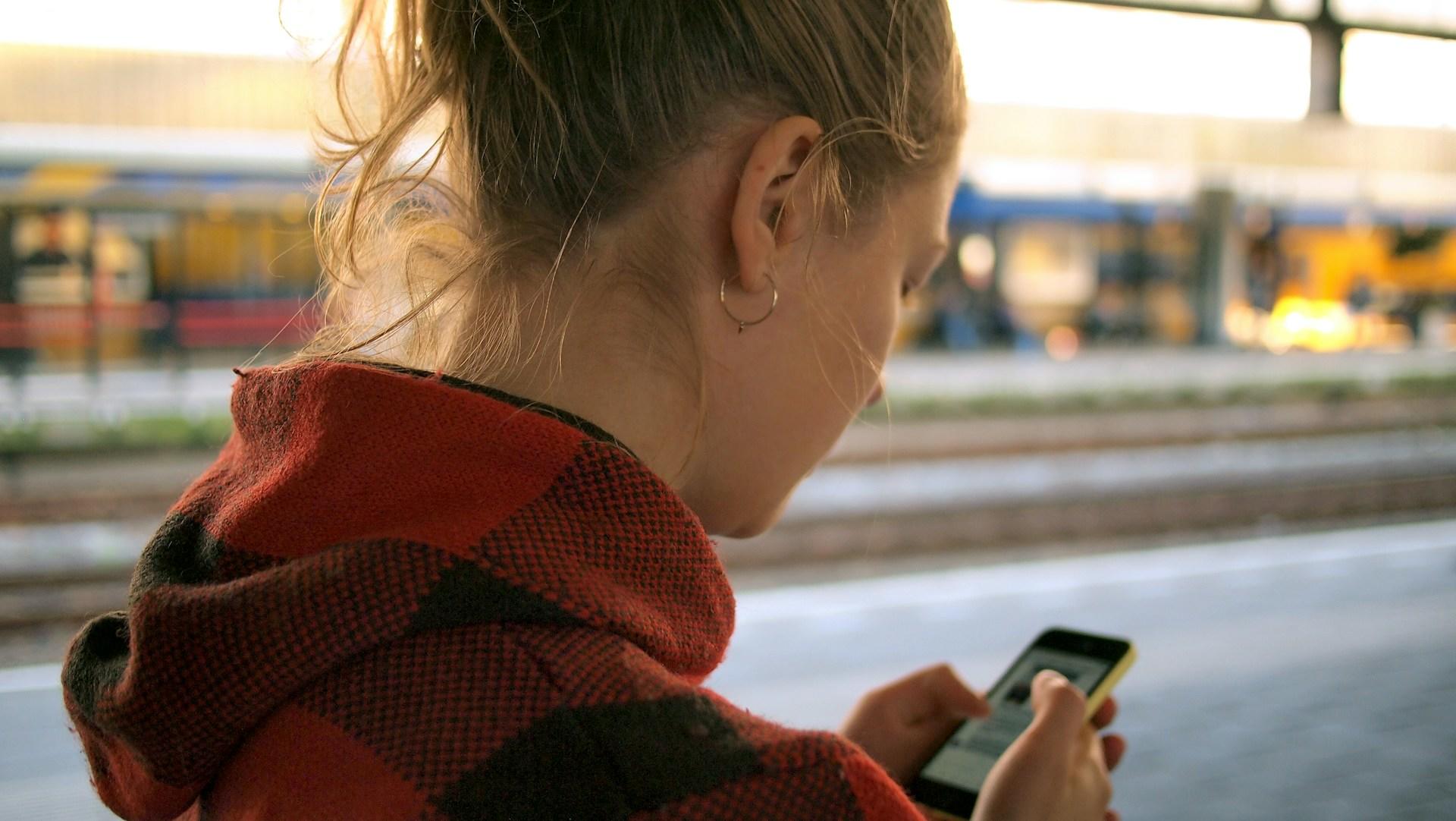 Dame står på togstasjon og ser på telefonen sin.