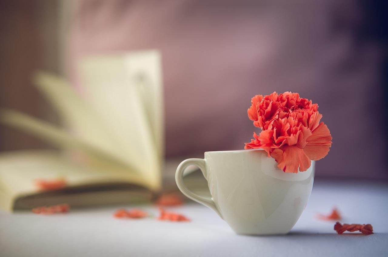 En kaffekopp med rød blomst oppi hvor du skimter en åpen bok i bakgrunnen