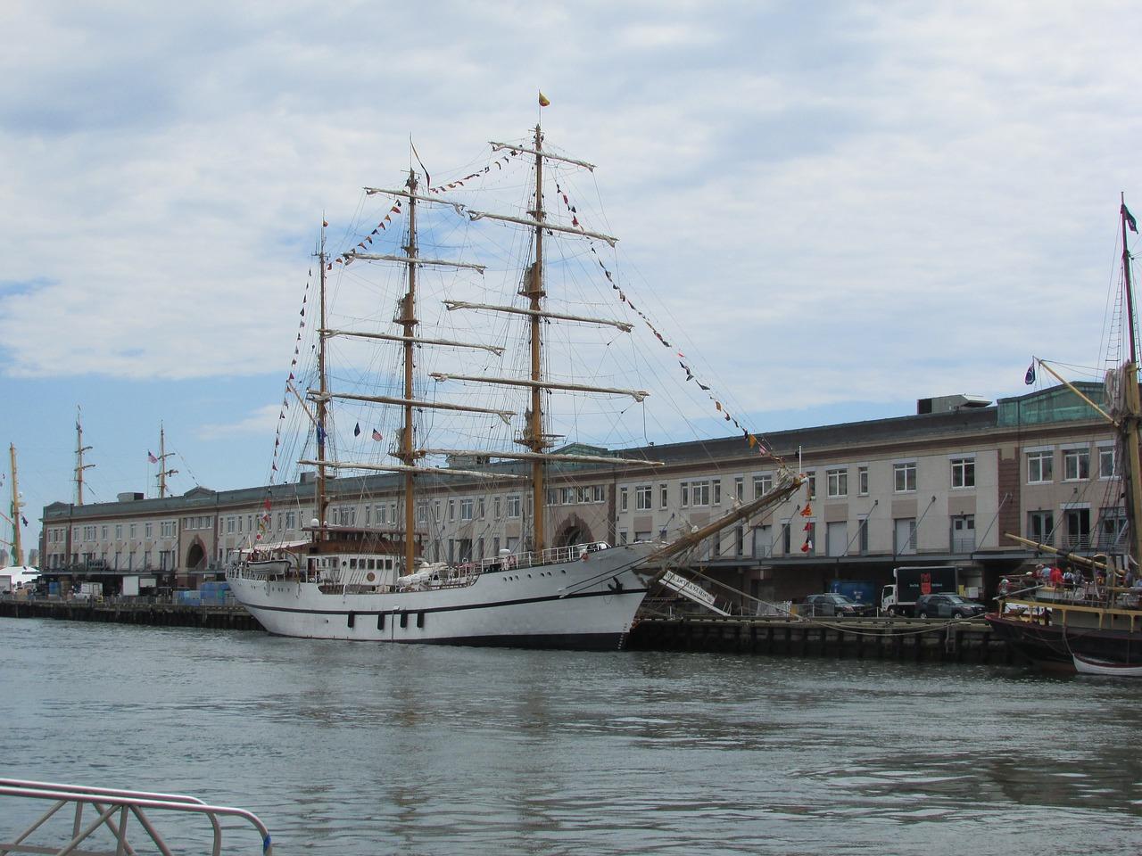 Et seilskip dokket ved en havn med bygninger i bakgrunnen.