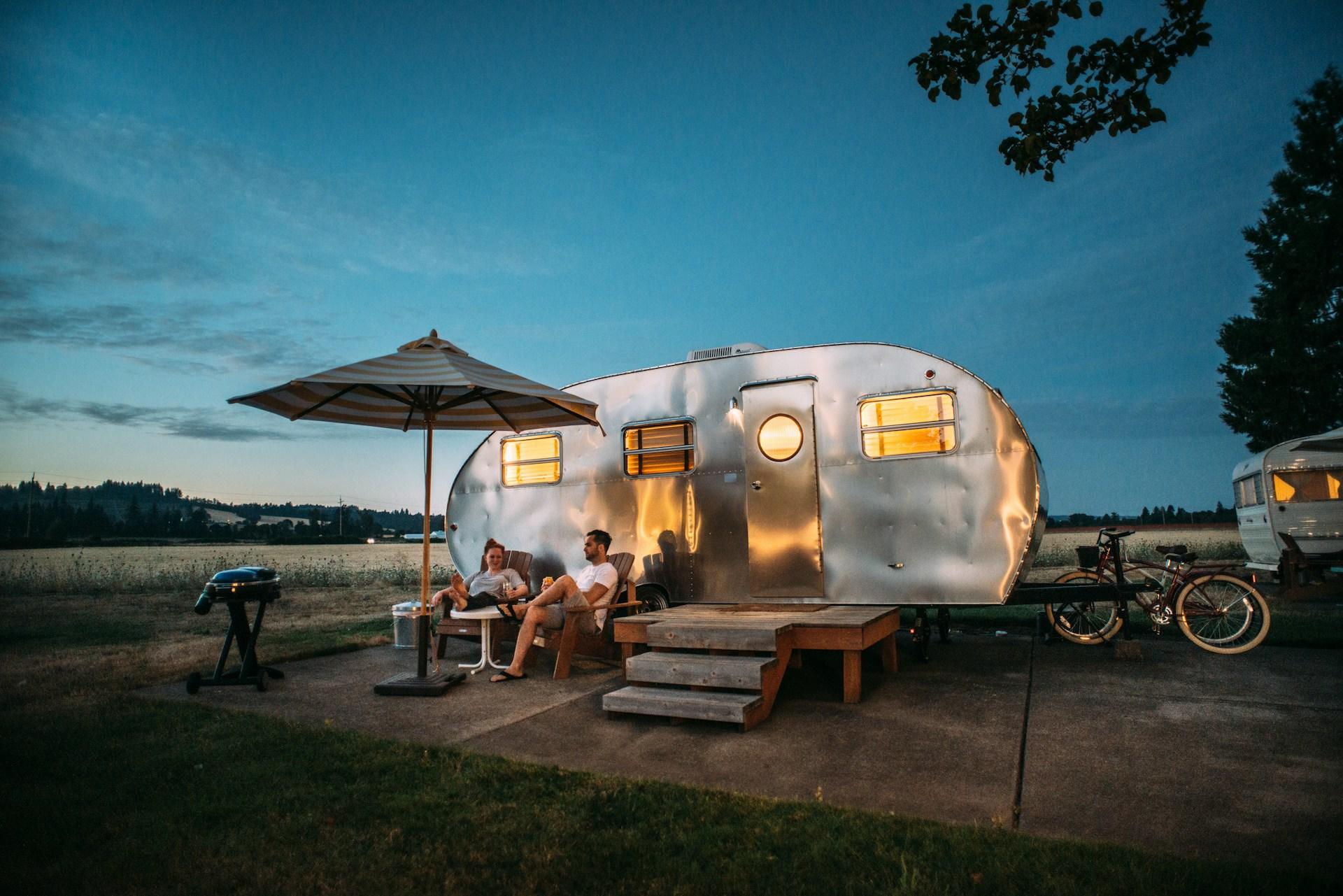 To mennesker sitter i hver sin stol utenfor sølvfarget campingvogn.