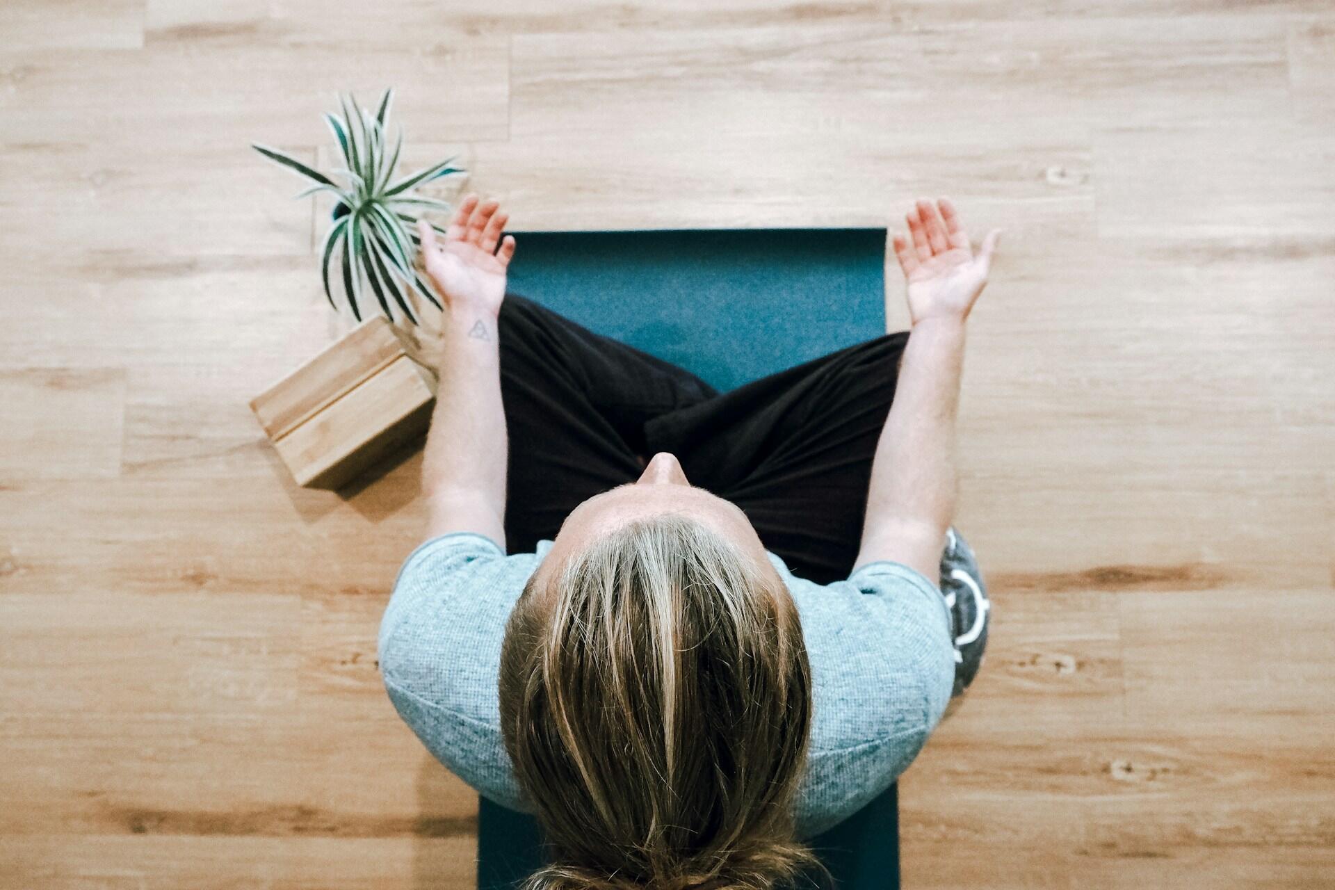 Person mediterer på yogamatte sett ovenfra, med hendene åpne og plante ved siden av