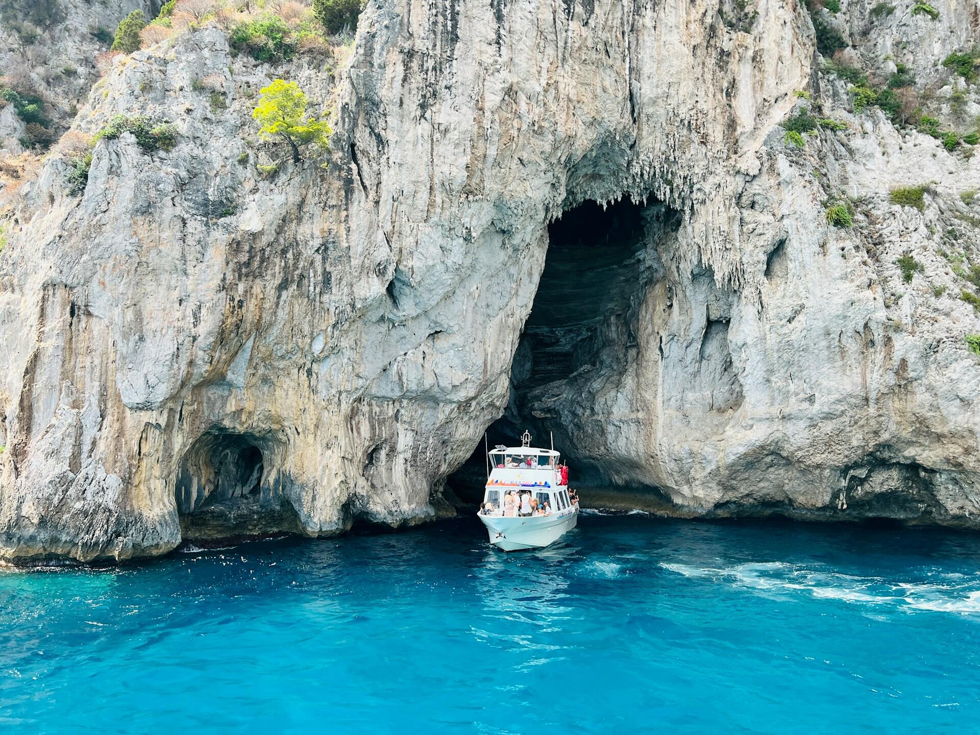 Turistbåt ved inngangen til en havgrotte på Capri med blått hav og kalksteinsfjell