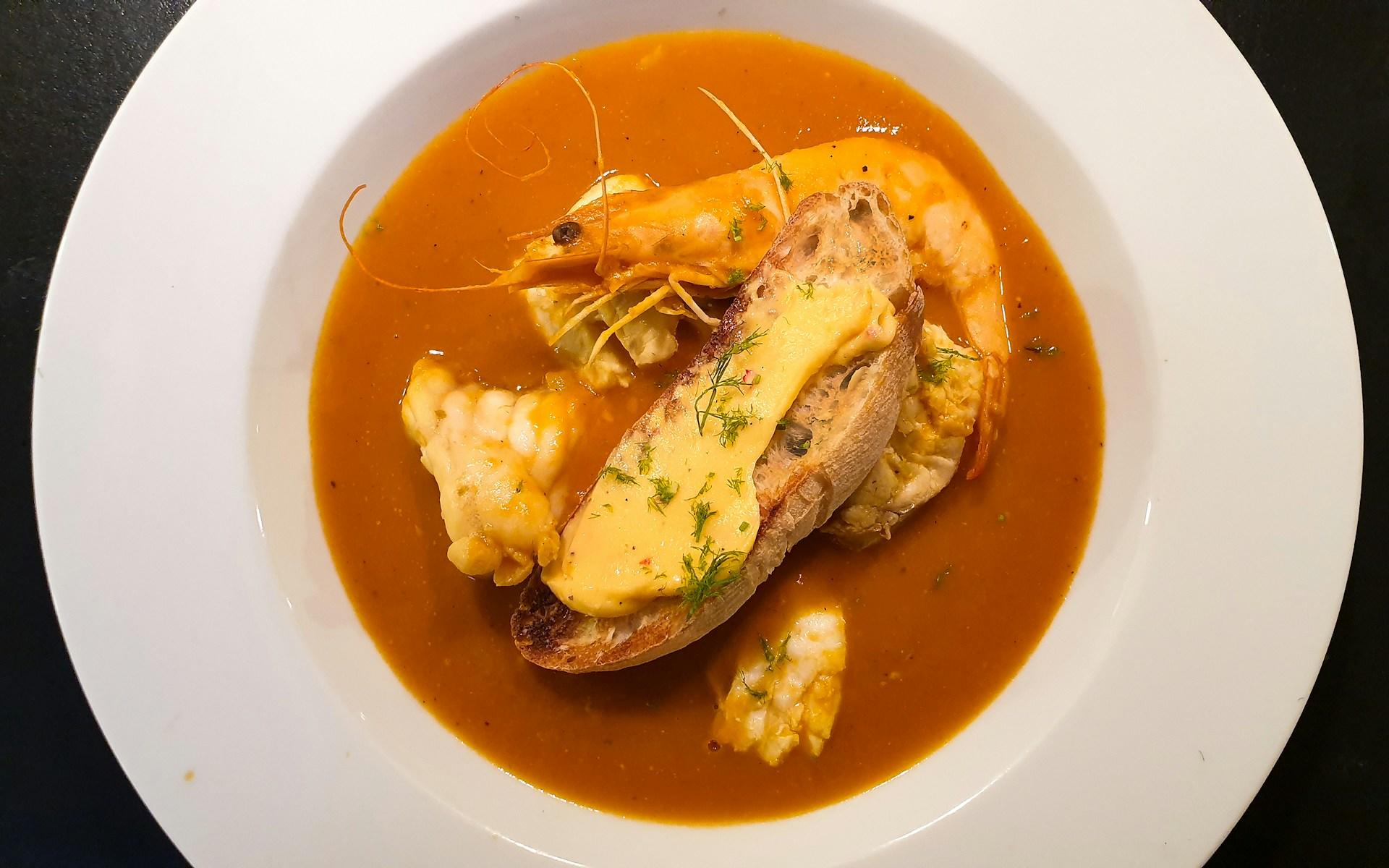 Oransje bouillabaisse med kreps i hvit skål.