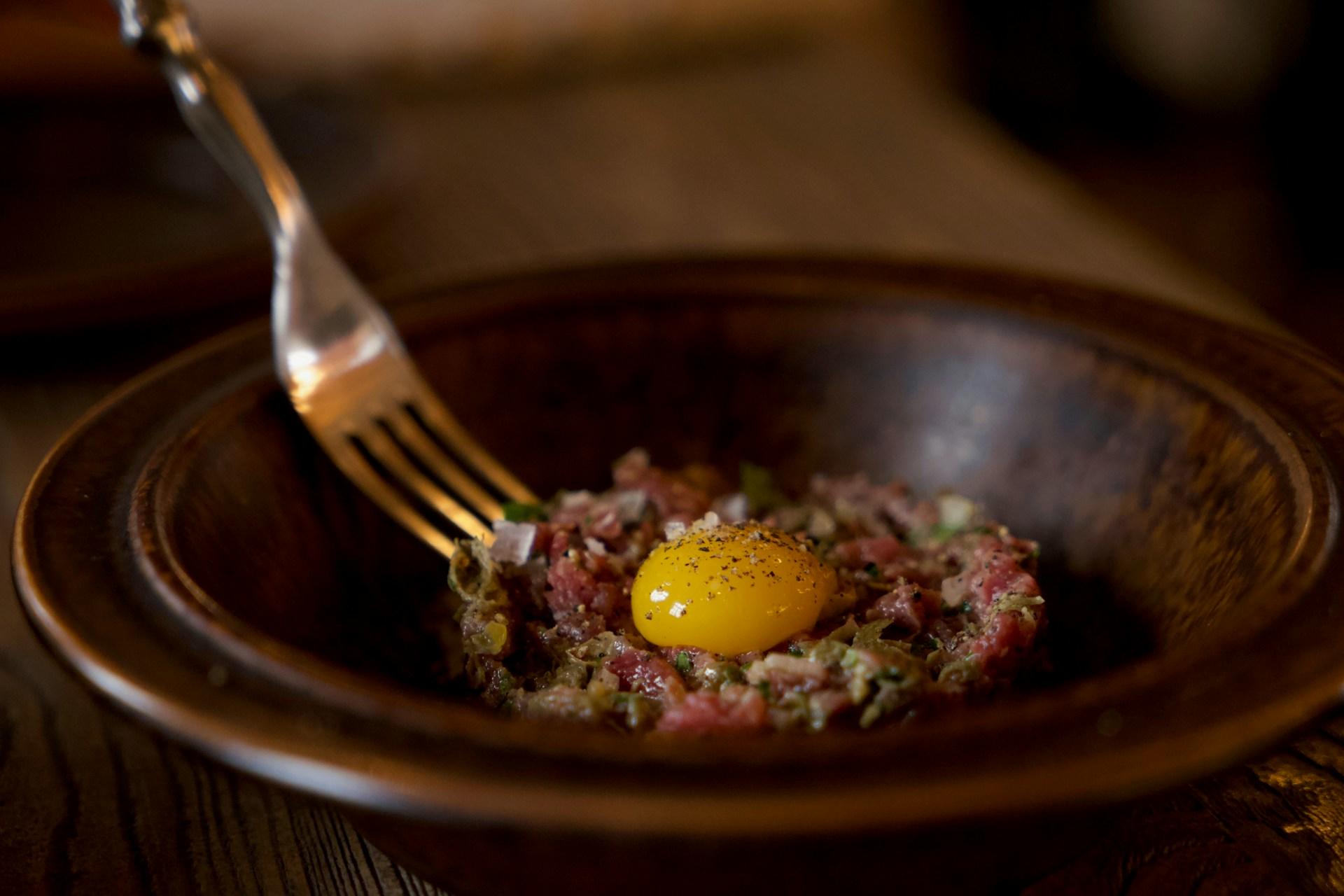 Tartar med eggeplomme på toppen i brun asjett.